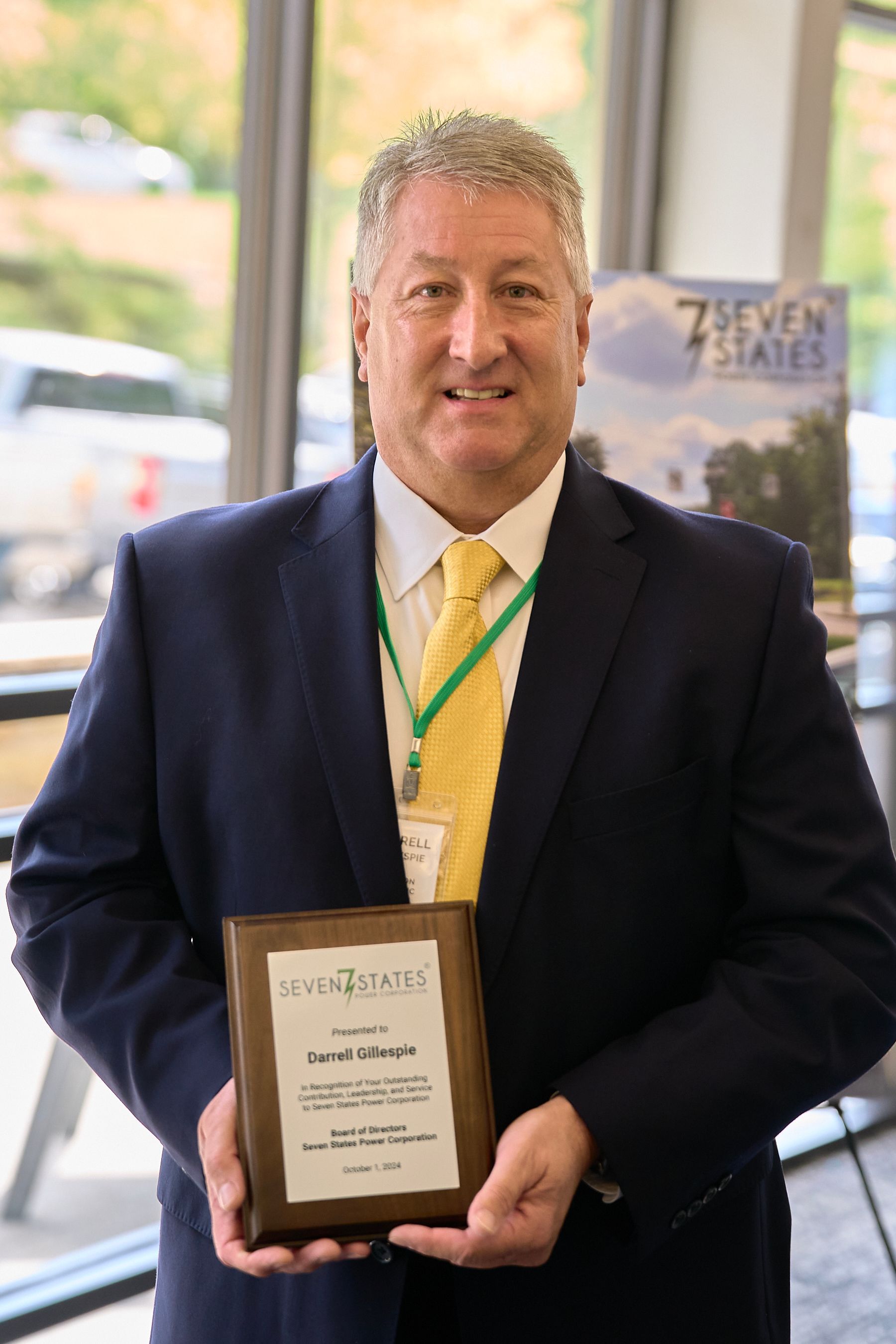 A man in a suit and tie is holding a wooden plaque.