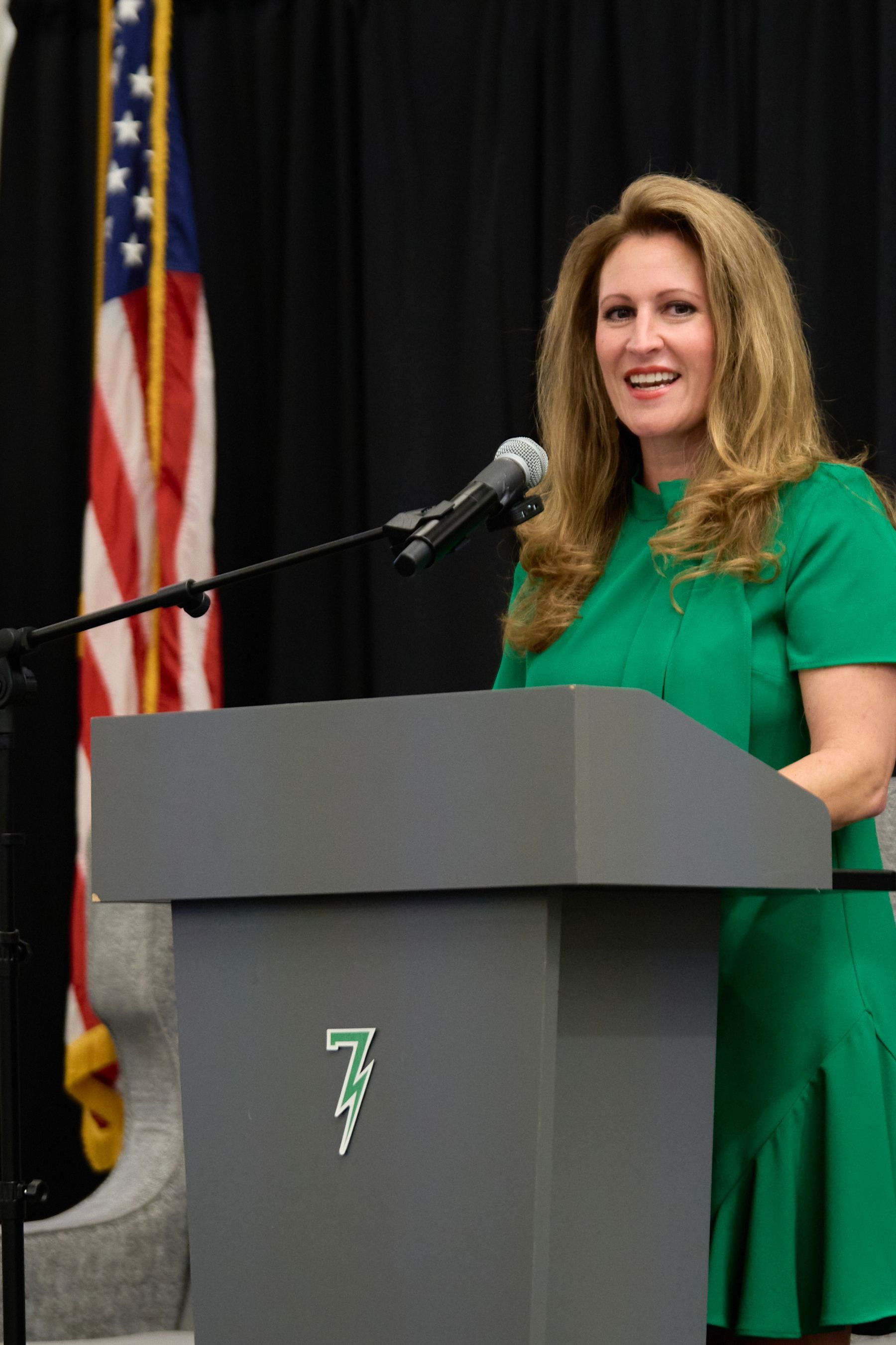 A woman in a green dress is standing at a podium speaking into a microphone.