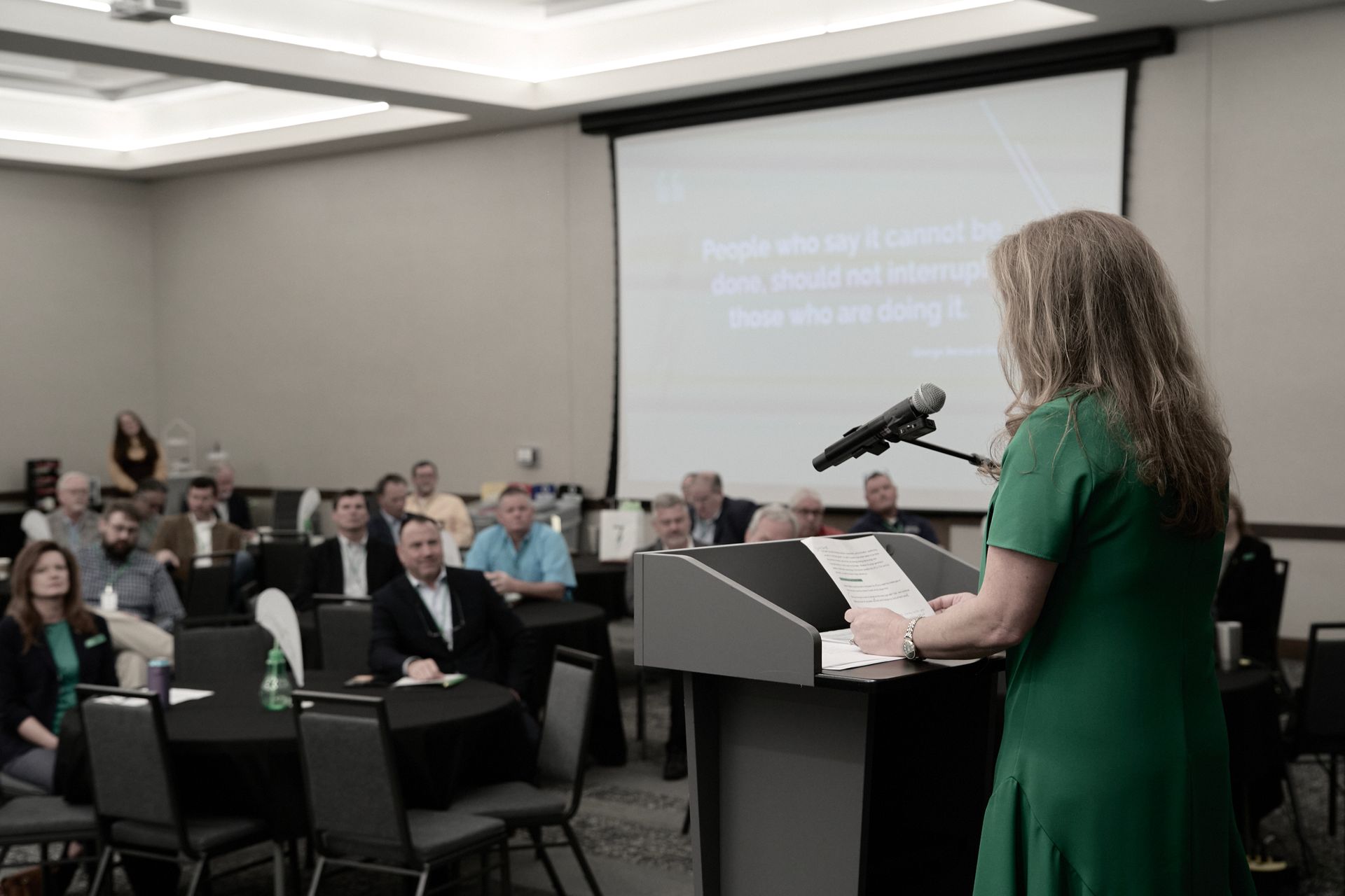A woman is standing at a podium giving a presentation to a group of people.