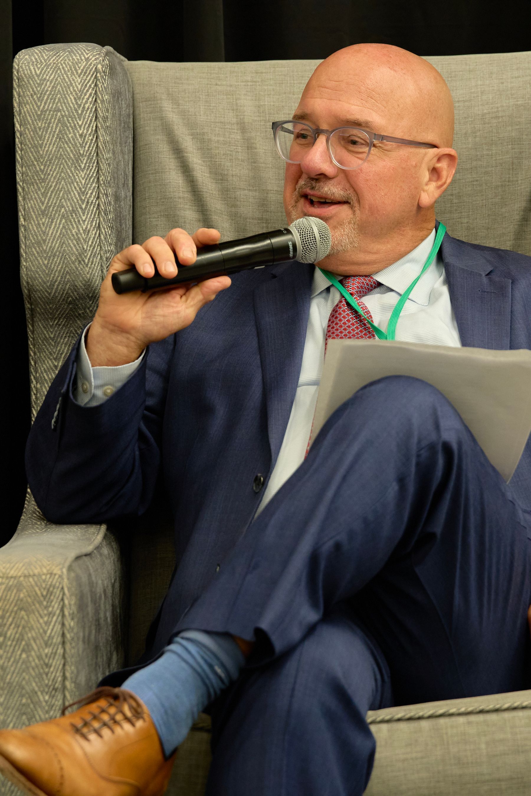 A man in a suit is sitting in a chair holding a microphone