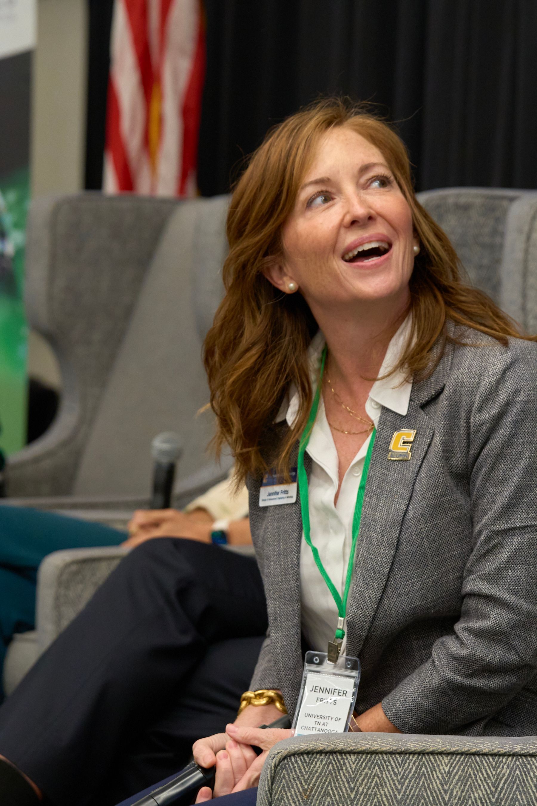 A woman in a suit is sitting in a chair and smiling.