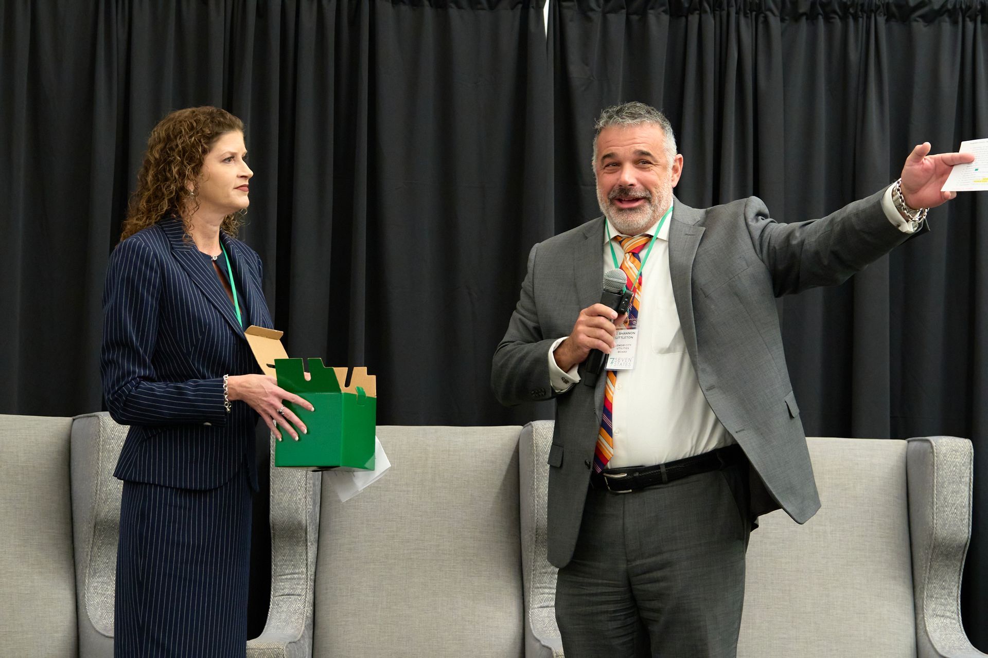 A man in a suit and tie is standing next to a woman holding a microphone.