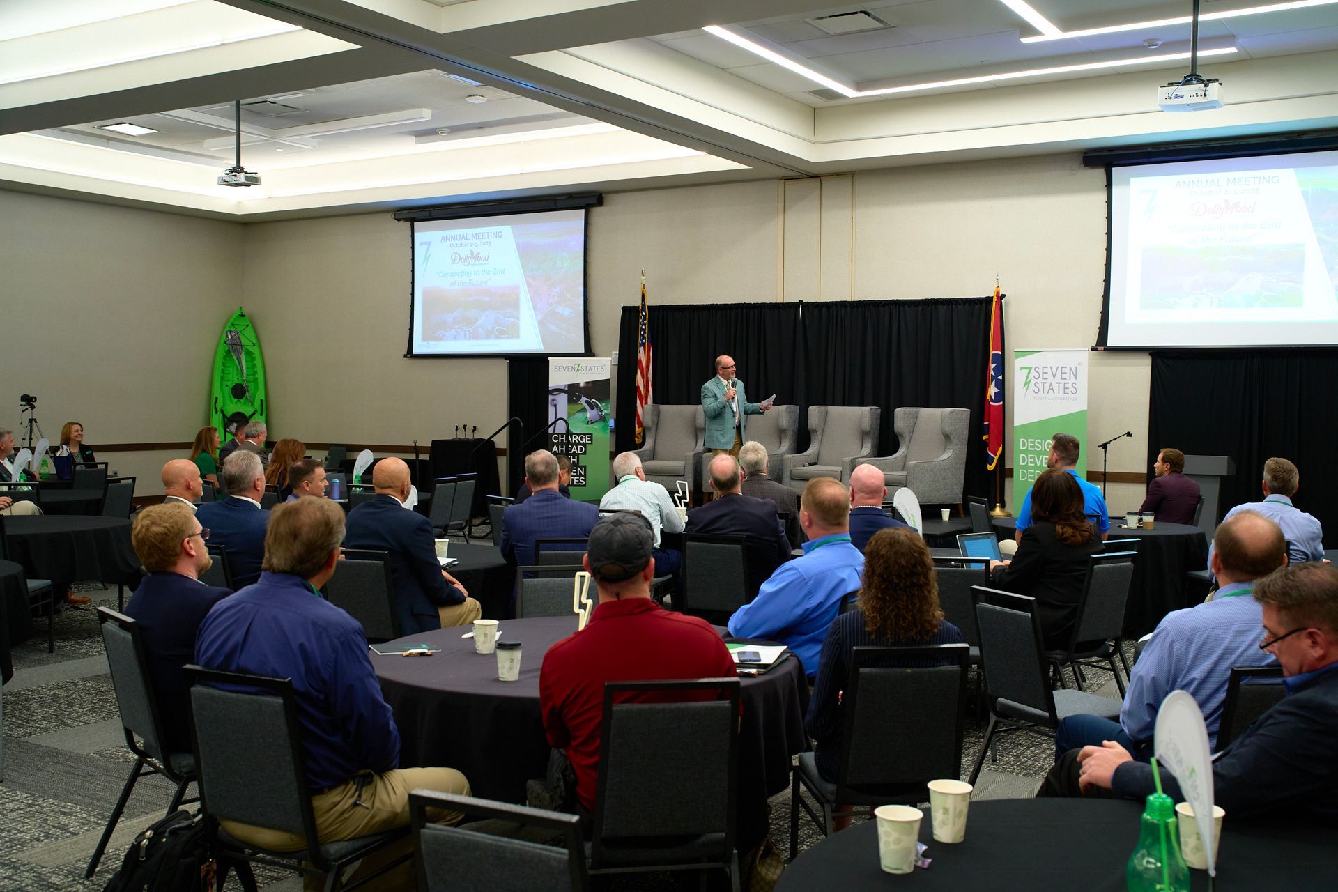 A group of people are sitting at tables in a conference room watching a presentation.