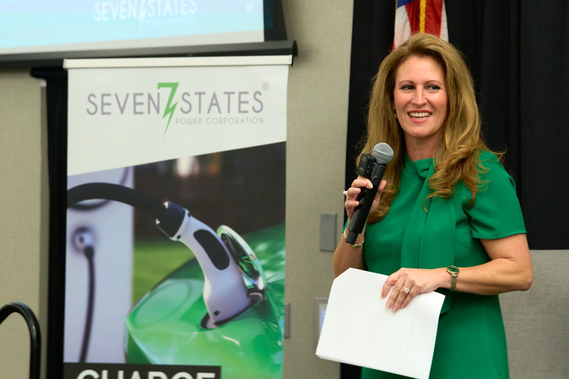 A woman in a green dress is holding a microphone in front of a seven states sign.