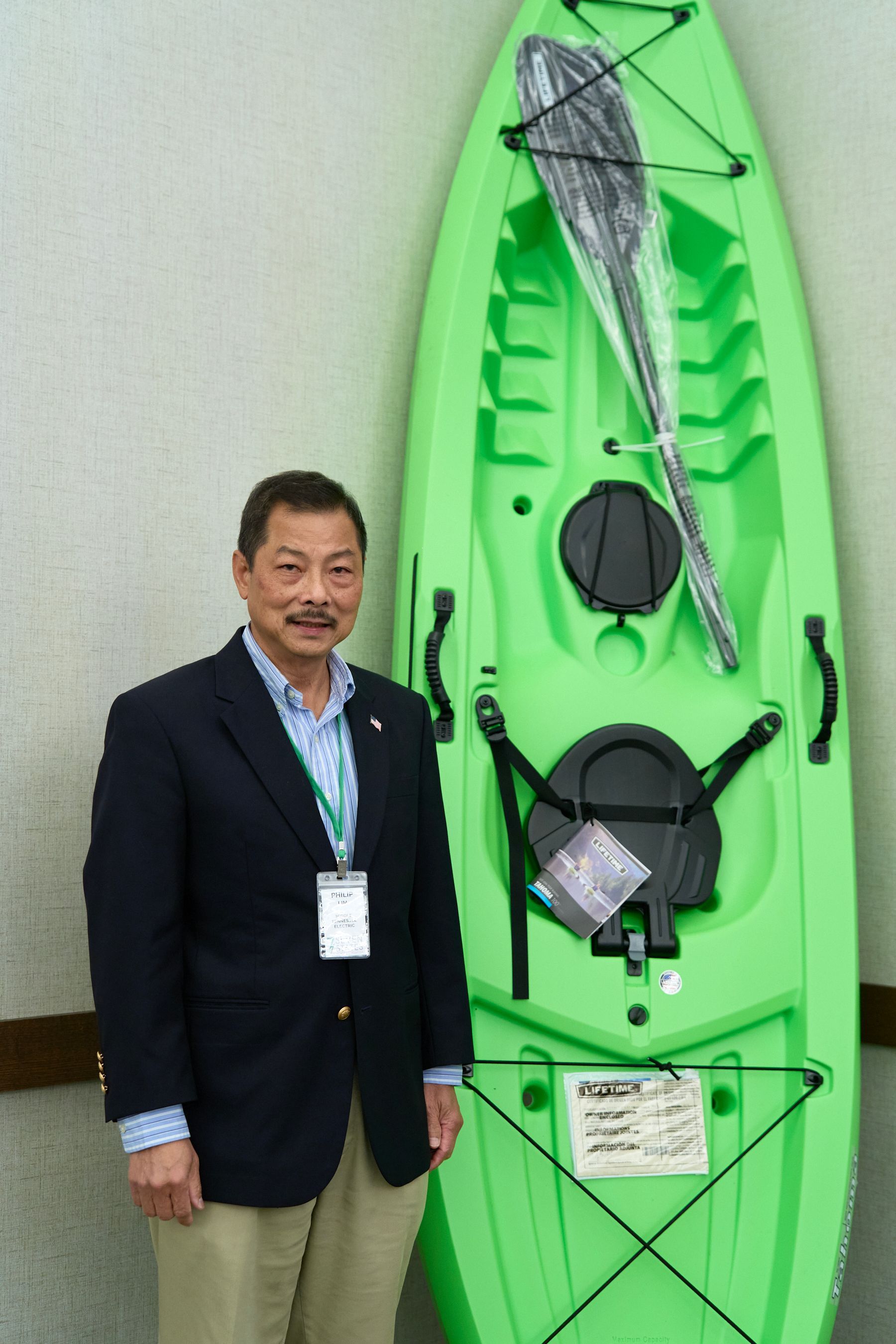 A man in a suit stands in front of a green kayak