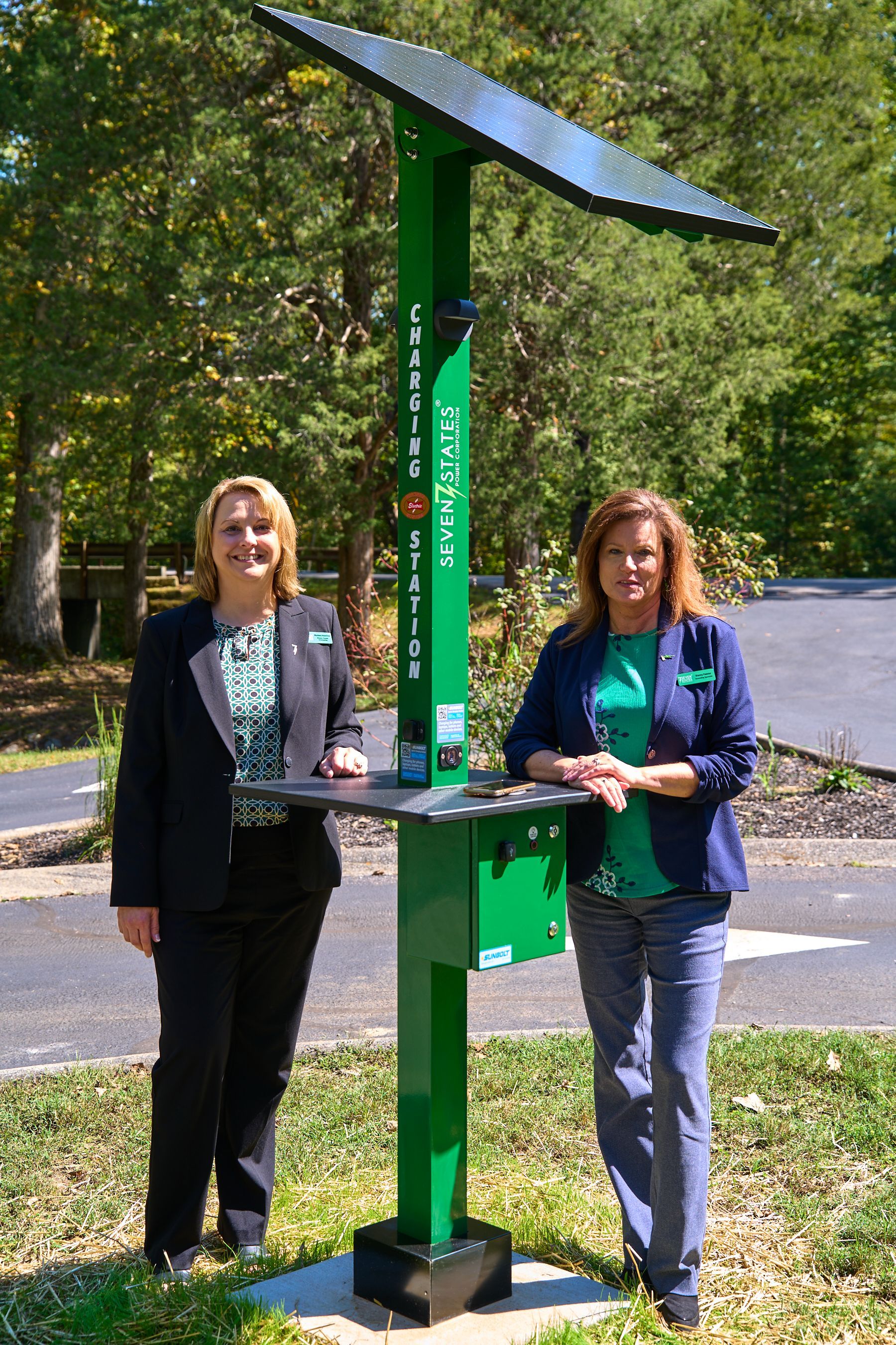 Two women are standing next to a green solar panel.