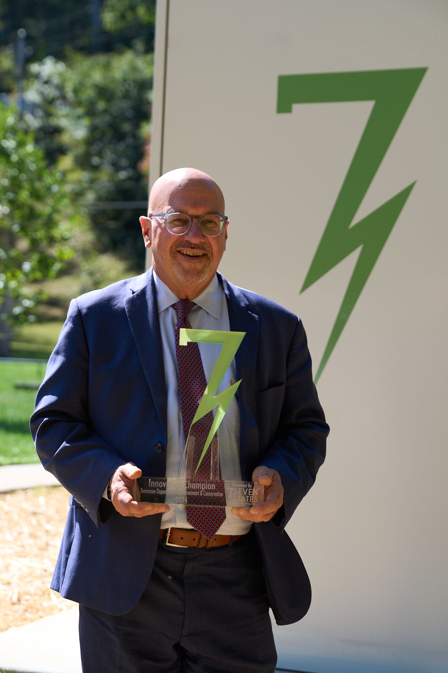 A man in a suit and tie is holding a trophy in front of a lightning bolt.