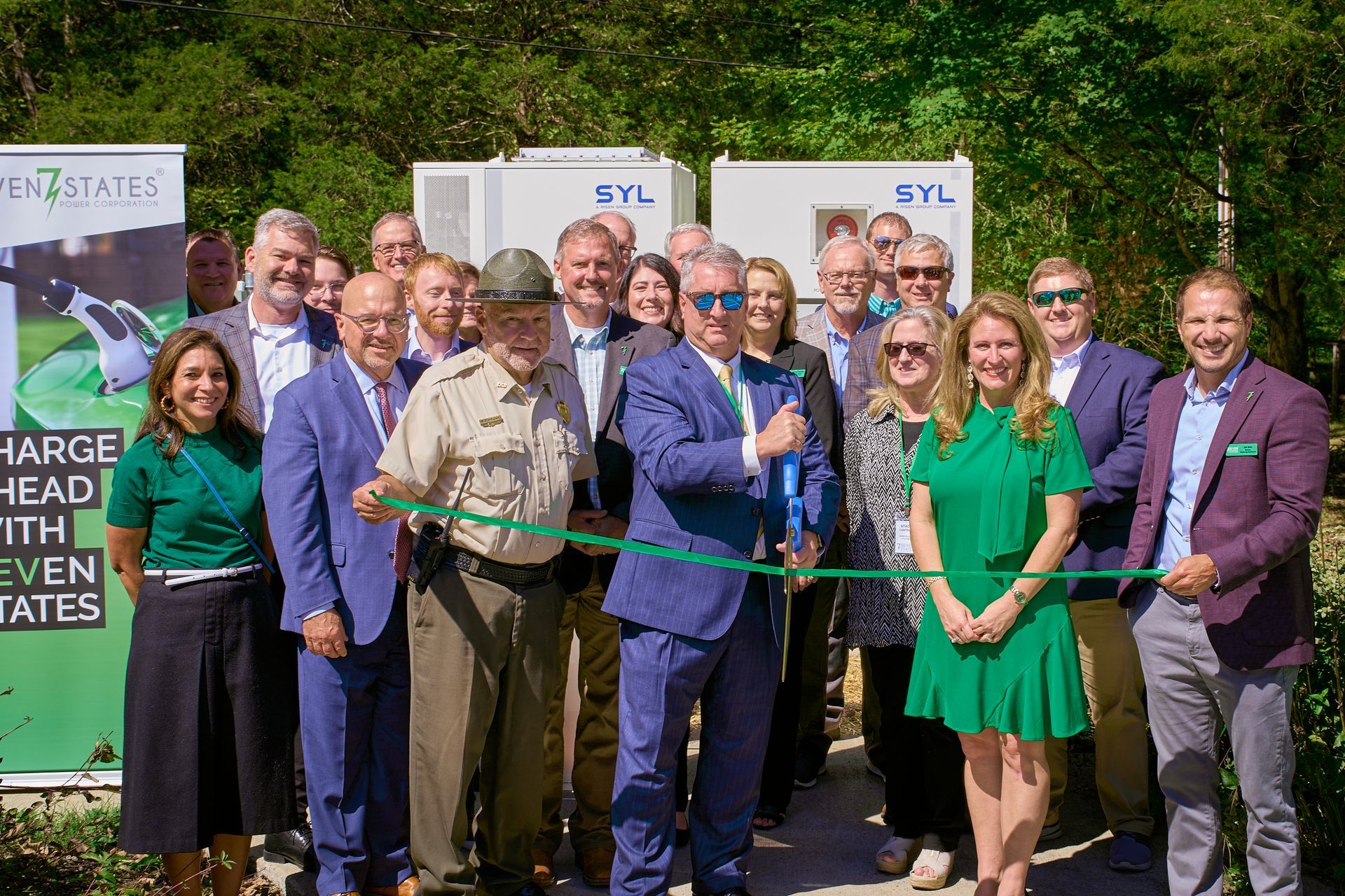 A group of people are standing next to each other cutting a green ribbon.
