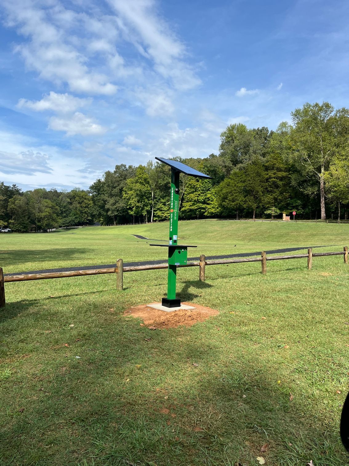 A green pole with a solar panel on top of it is in the middle of a grassy field.