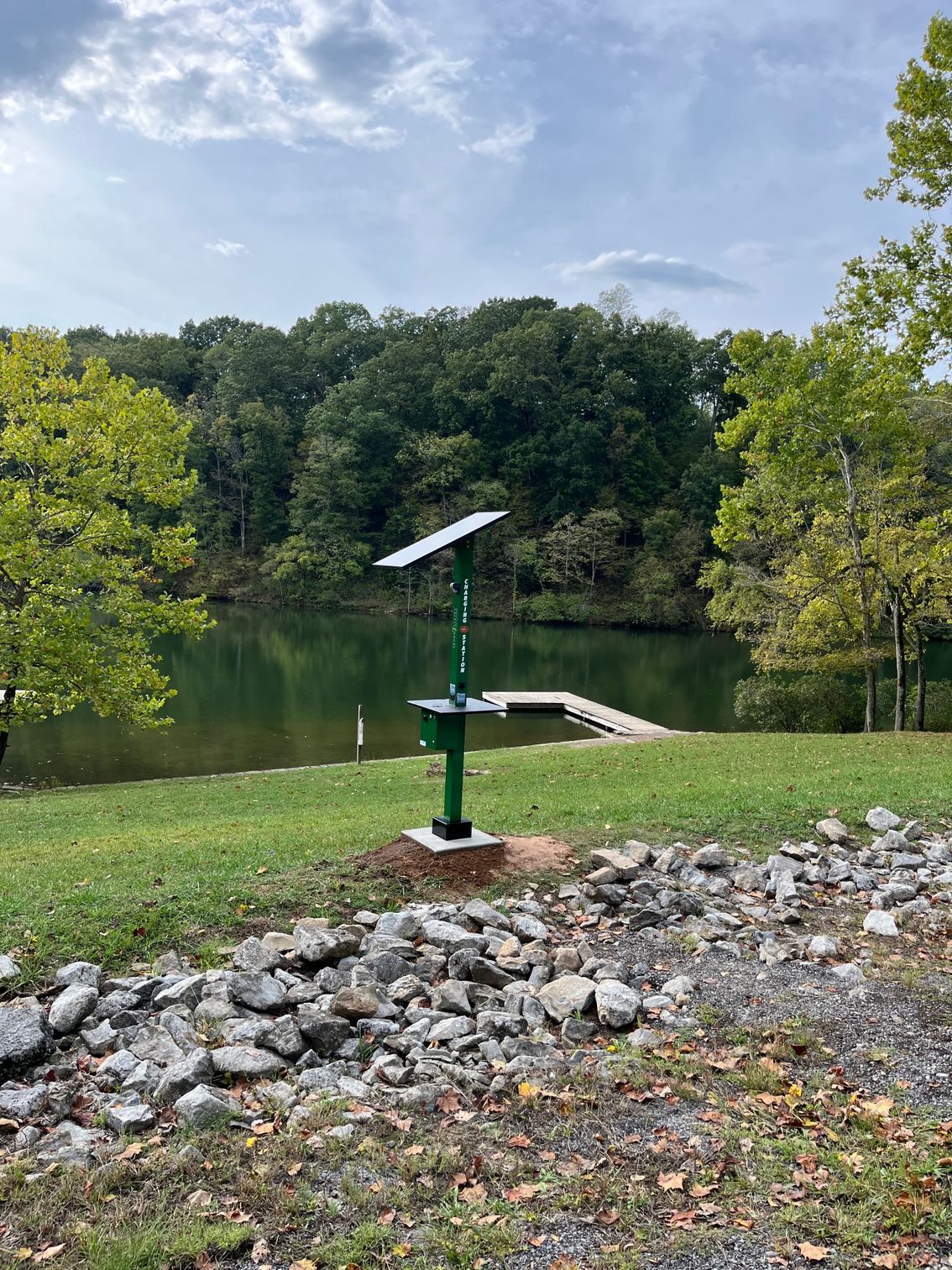 A green bench with a solar panel on top of it is sitting next to a lake.