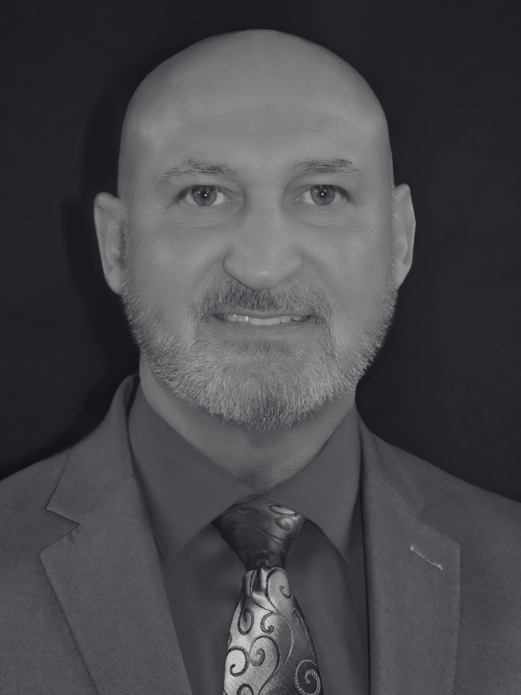A man in a suit and tie is smiling in a black and white photo.