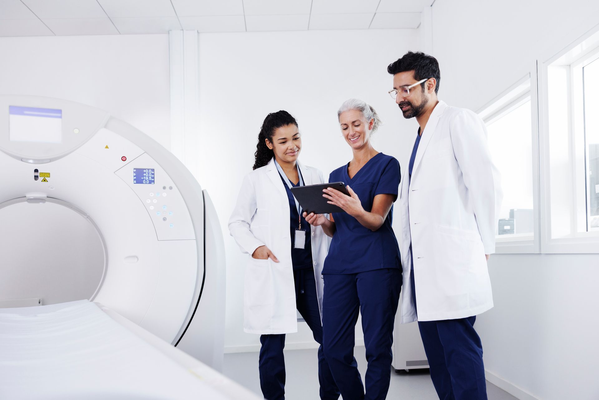 Three healthcare workers in conversation in a CAT scanner room Three healthcare workers in conversation in a CAT scanner room
