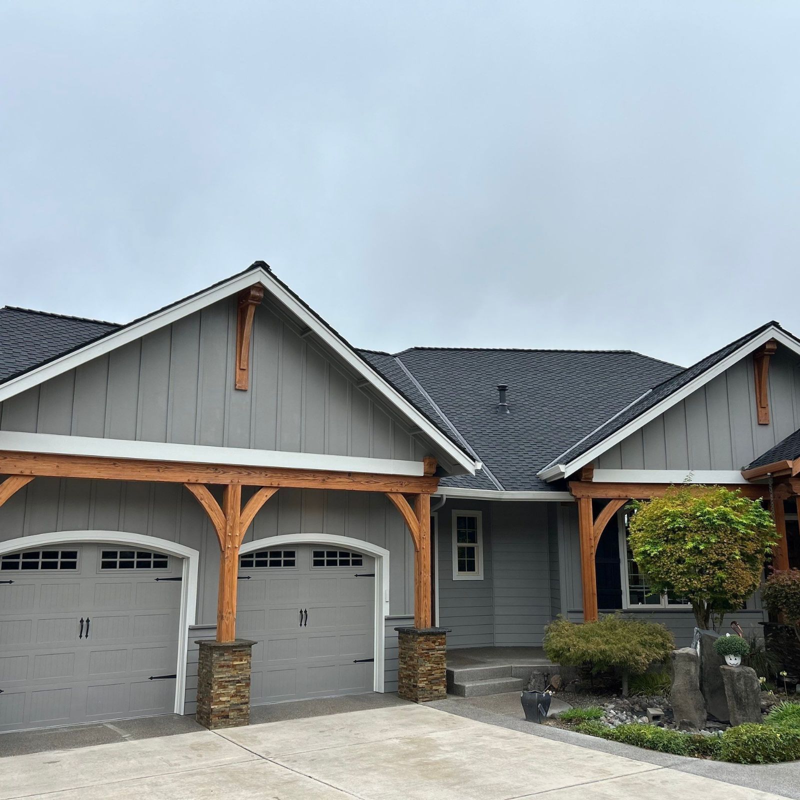 An aerial view of a blue house with a gray shingled roof, featuring several chimneys, vents, and a small patio area.