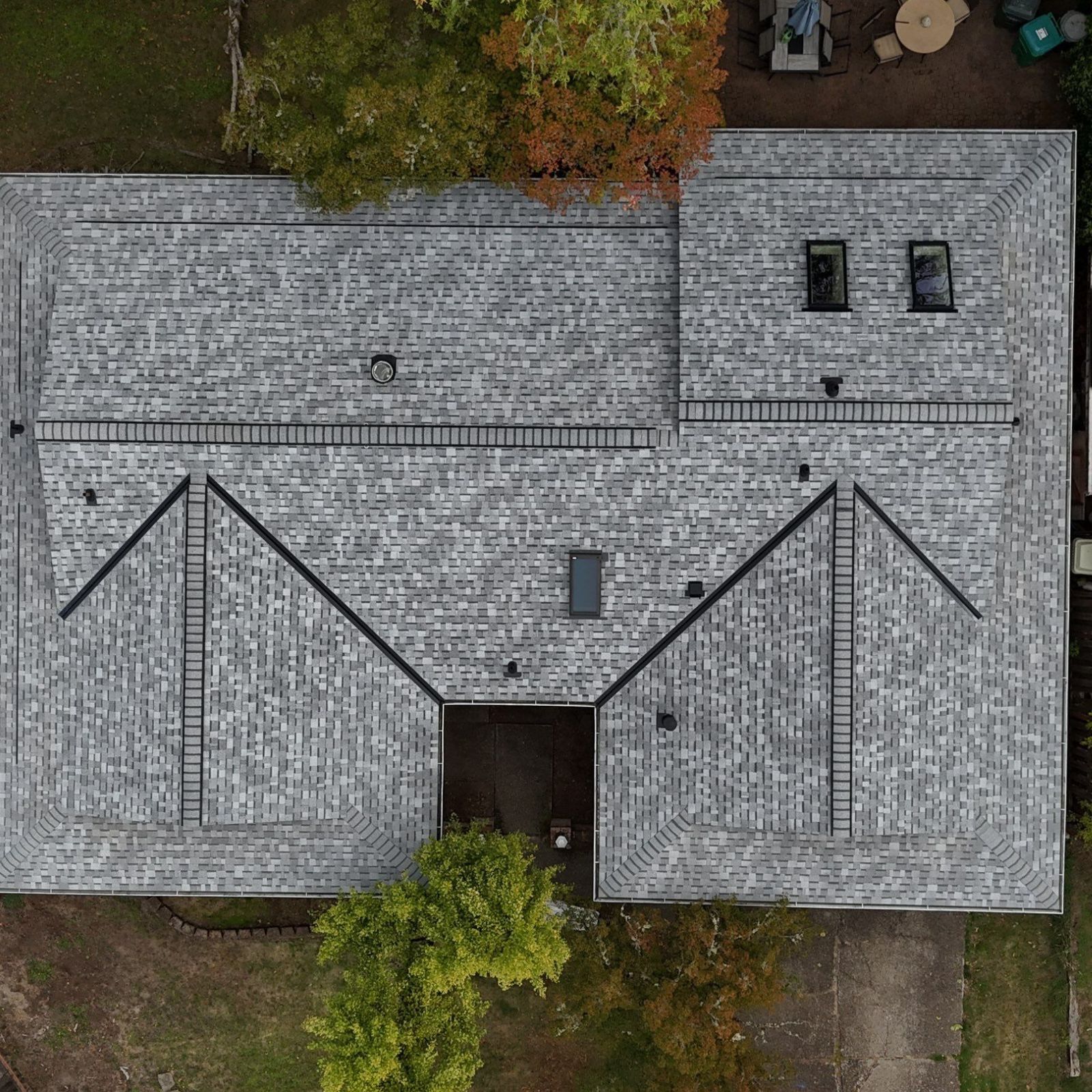 A high-angle view of a house roof with dark shingles, several skylights, a white gable with fish-scale siding, and a car.