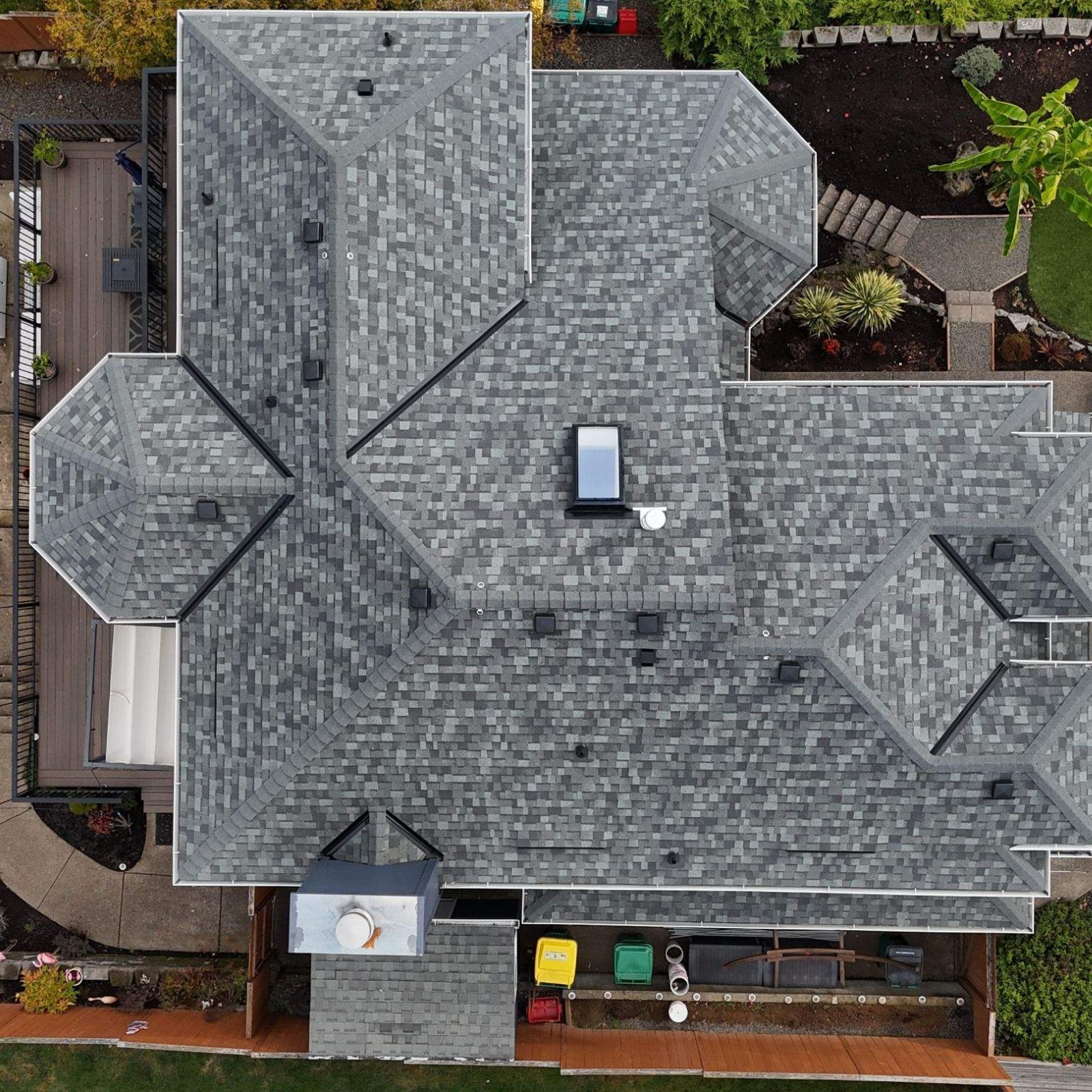 An aerial view of a dark grey shingled roof with several black vents on a two-story home with dark grey siding.
