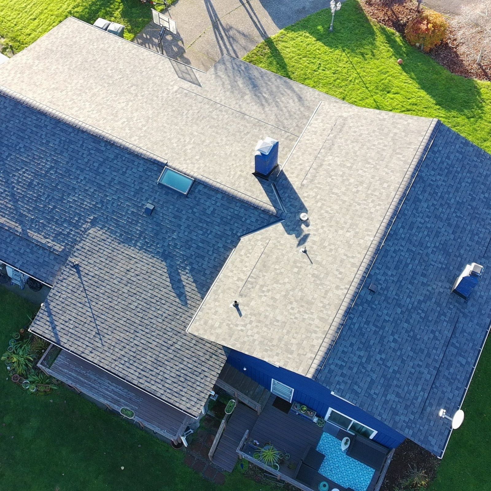 Aerial view of a residential grey shingled roof with multiple vents and a red accent section near a brick chimney.