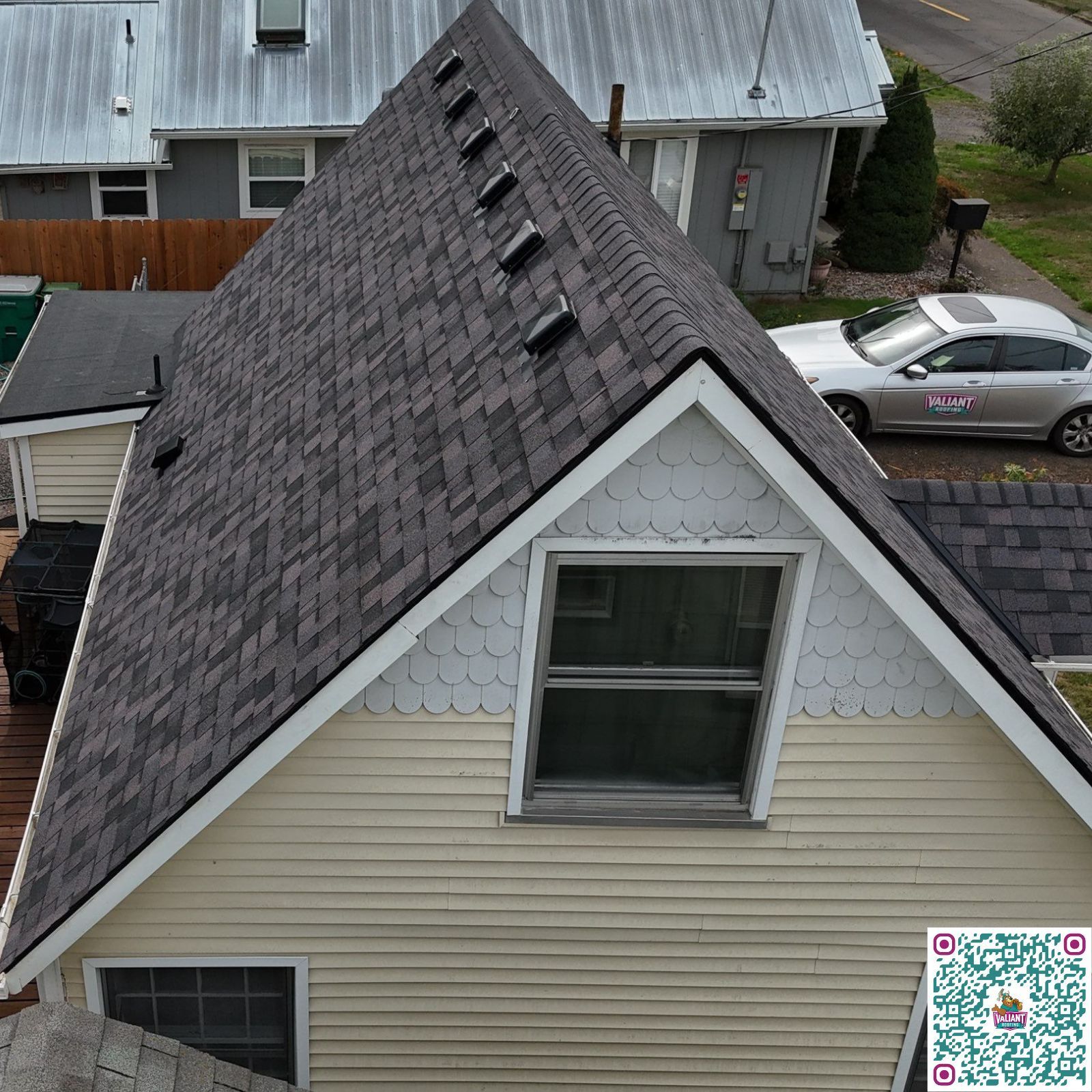Aerial view of a large house with a gray shingled roof, arched entryway, palm tree, and brick driveway.