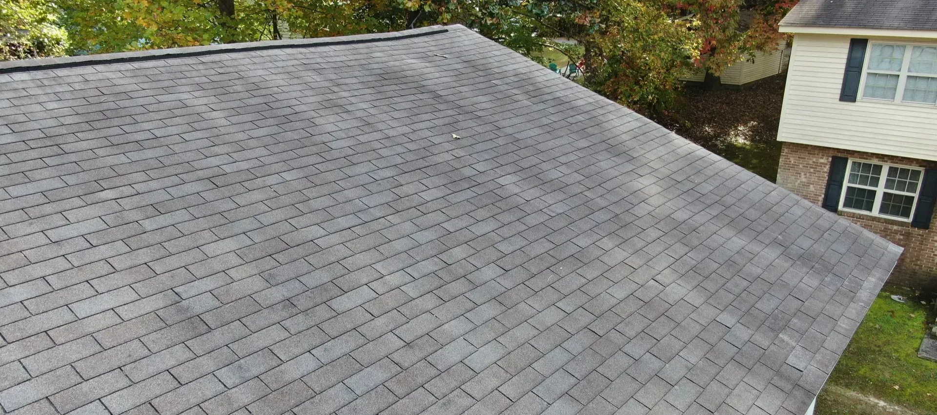 Overhead view of a gray asphalt shingle roof. Adjacent is a two-story home with a white exterior.