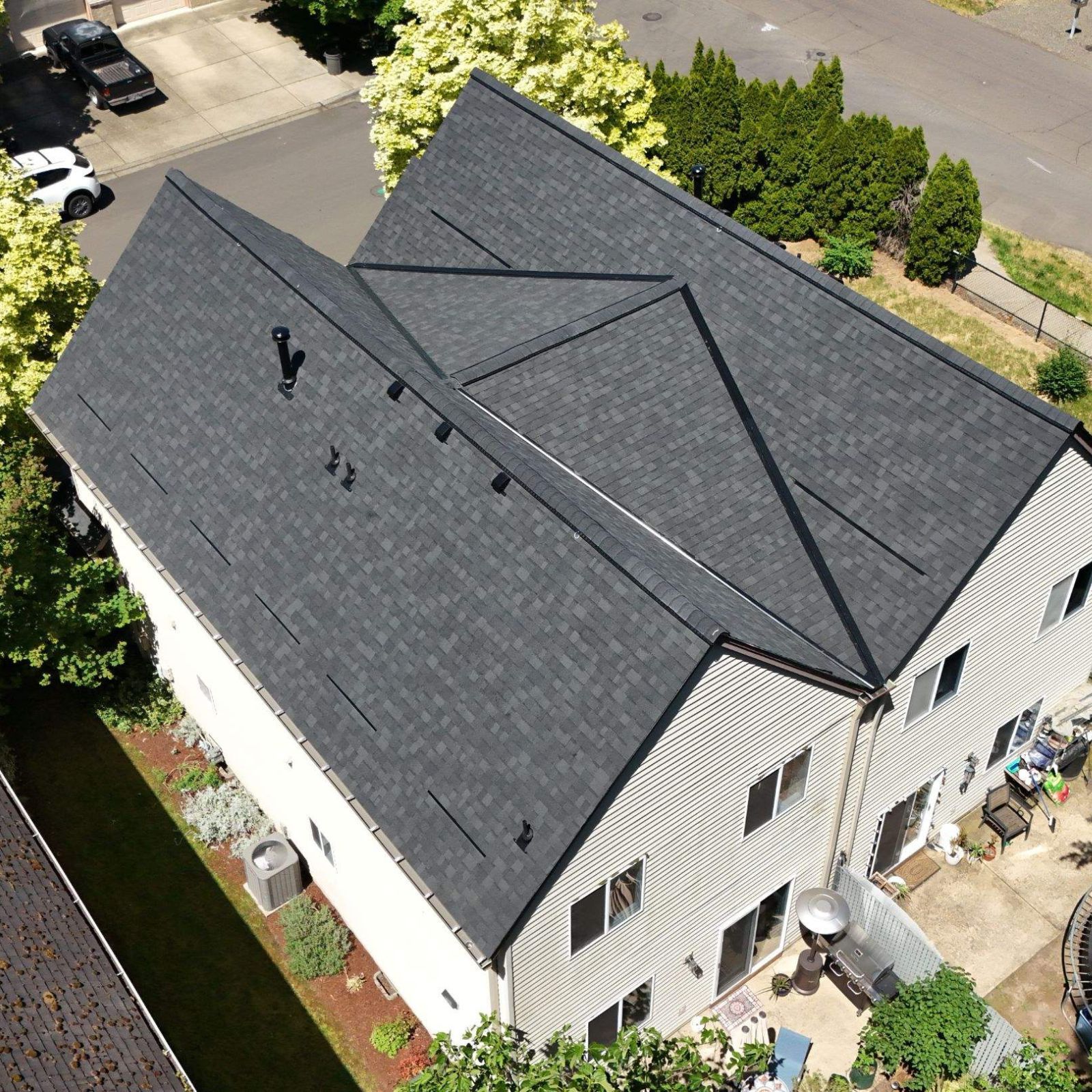 High-angle, aerial view of a tan two-story house with a grey shingled roof, featuring a front porch and red foliage.
