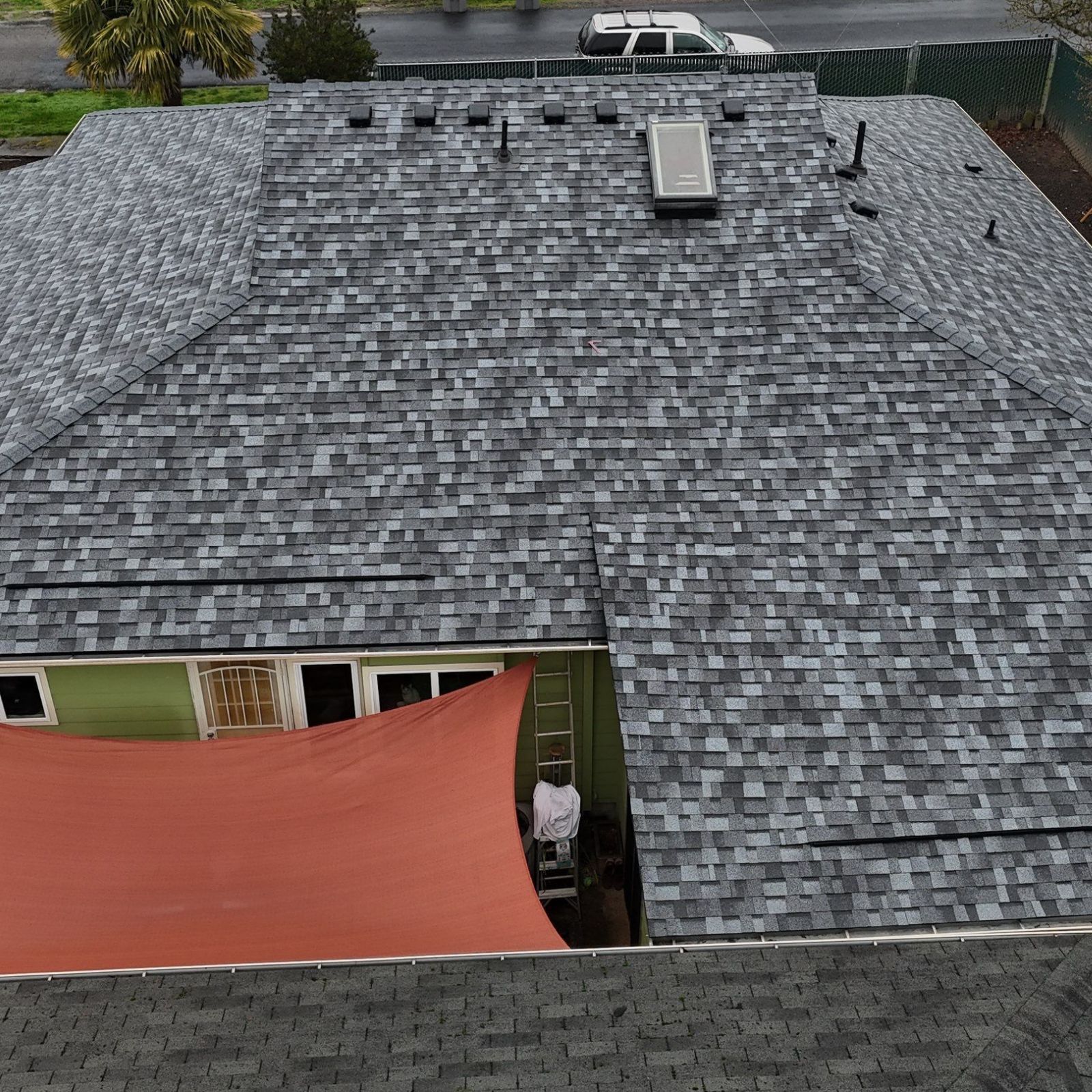An aerial view of a multi-sectioned house roof with grey shingles, a section of red corrugated roofing, and a chimney.