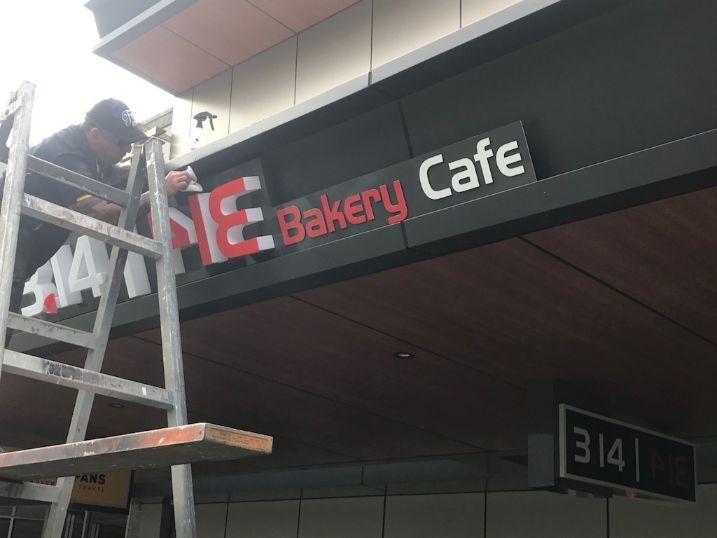 A Man Is Working On A Sign For A Bakery Cafe — Cairns Signcorp In Portsmith, QLD