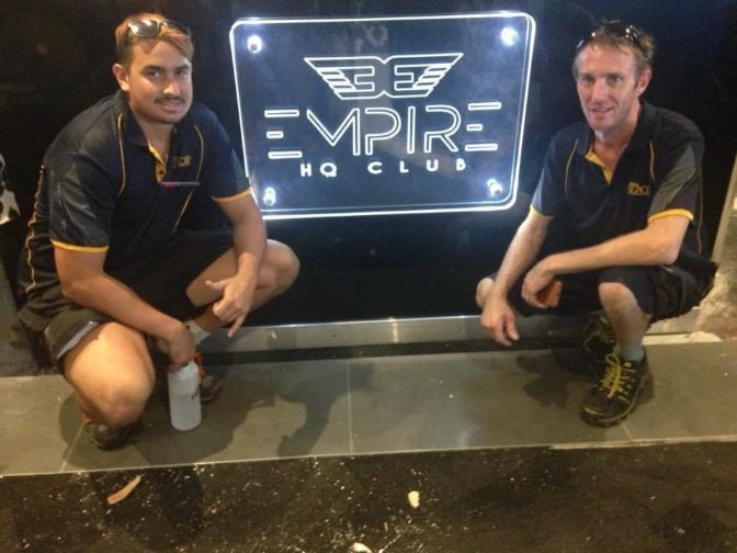 Two Men Squatting In Front Of A Sign That Says Empire — Cairns Signcorp In Portsmith, QLD