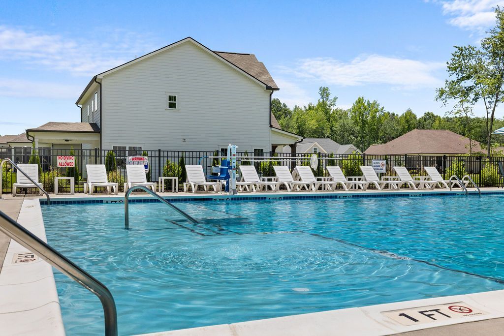 A large swimming pool with chairs and a house in the background.
