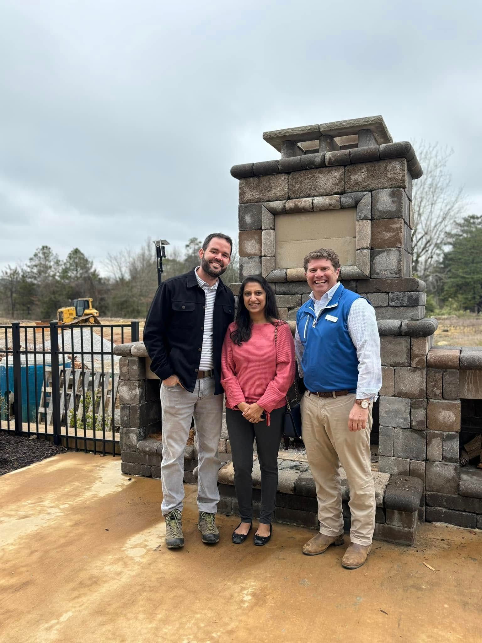 Three people are standing in front of a stone fireplace.