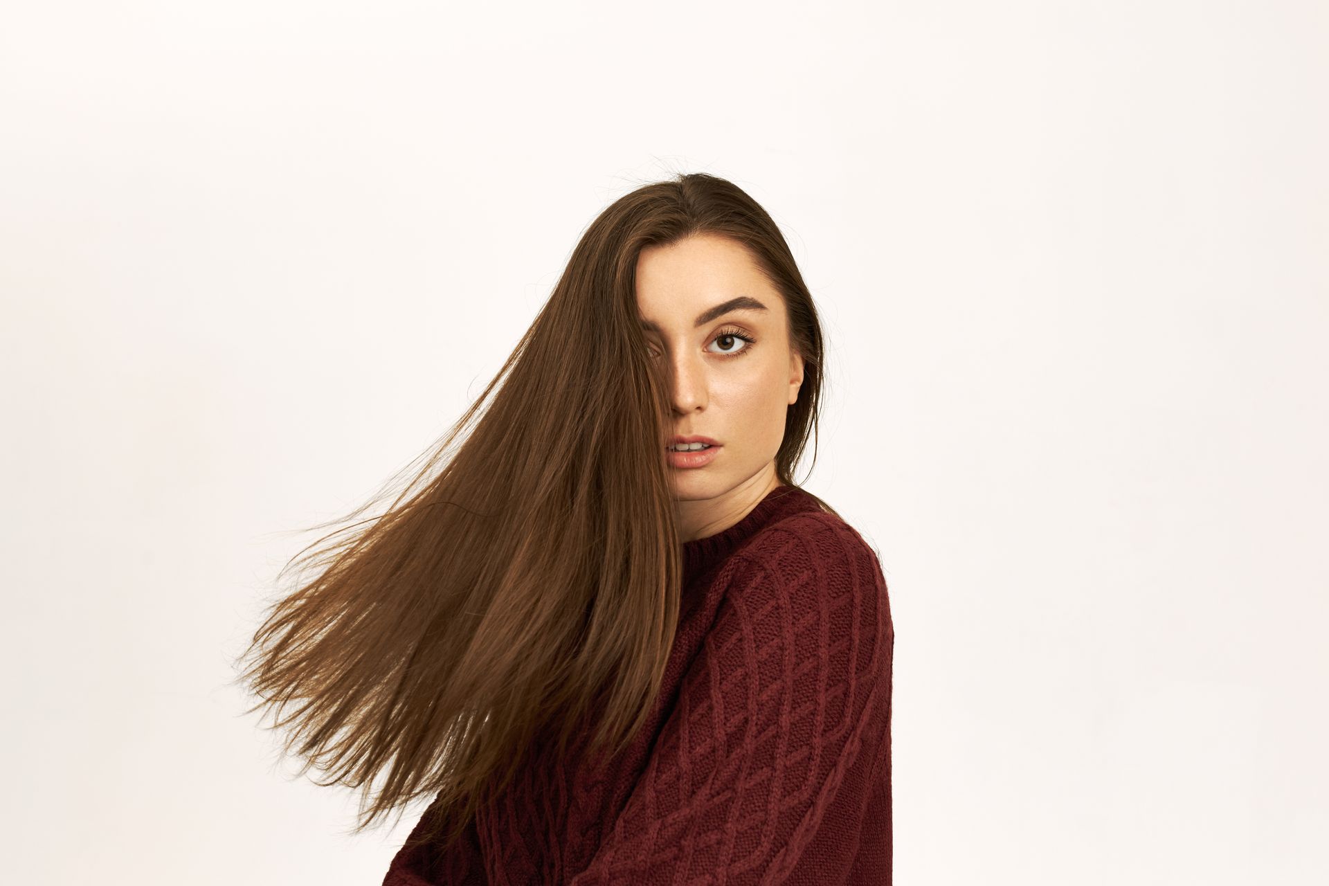 A woman in a maroon sweater with long hair blowing in the wind.