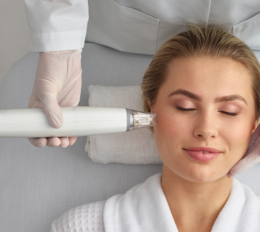 A woman in a white robe is getting a treatment on her face.