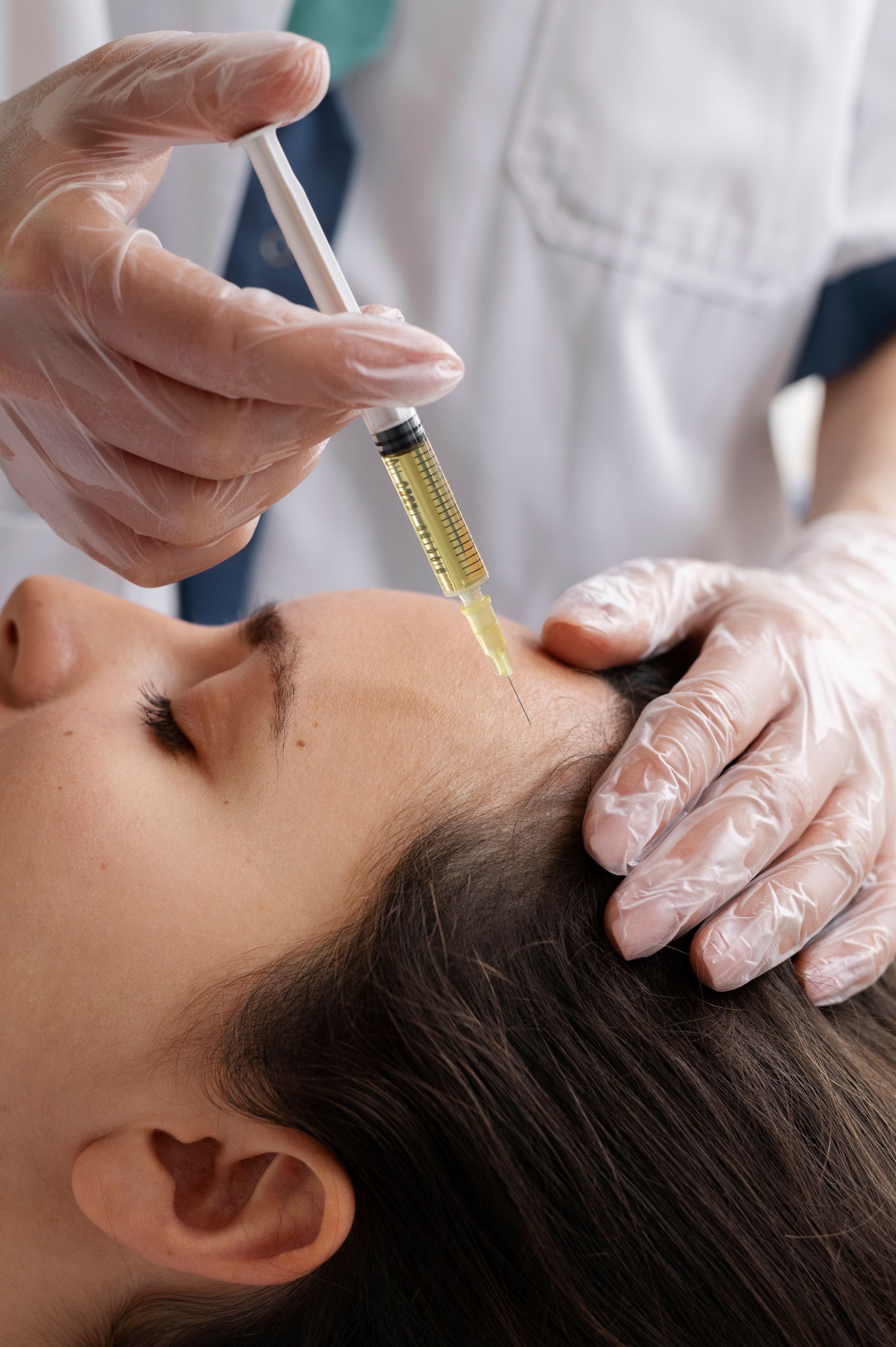 A woman is getting an injection in her forehead by a doctor.