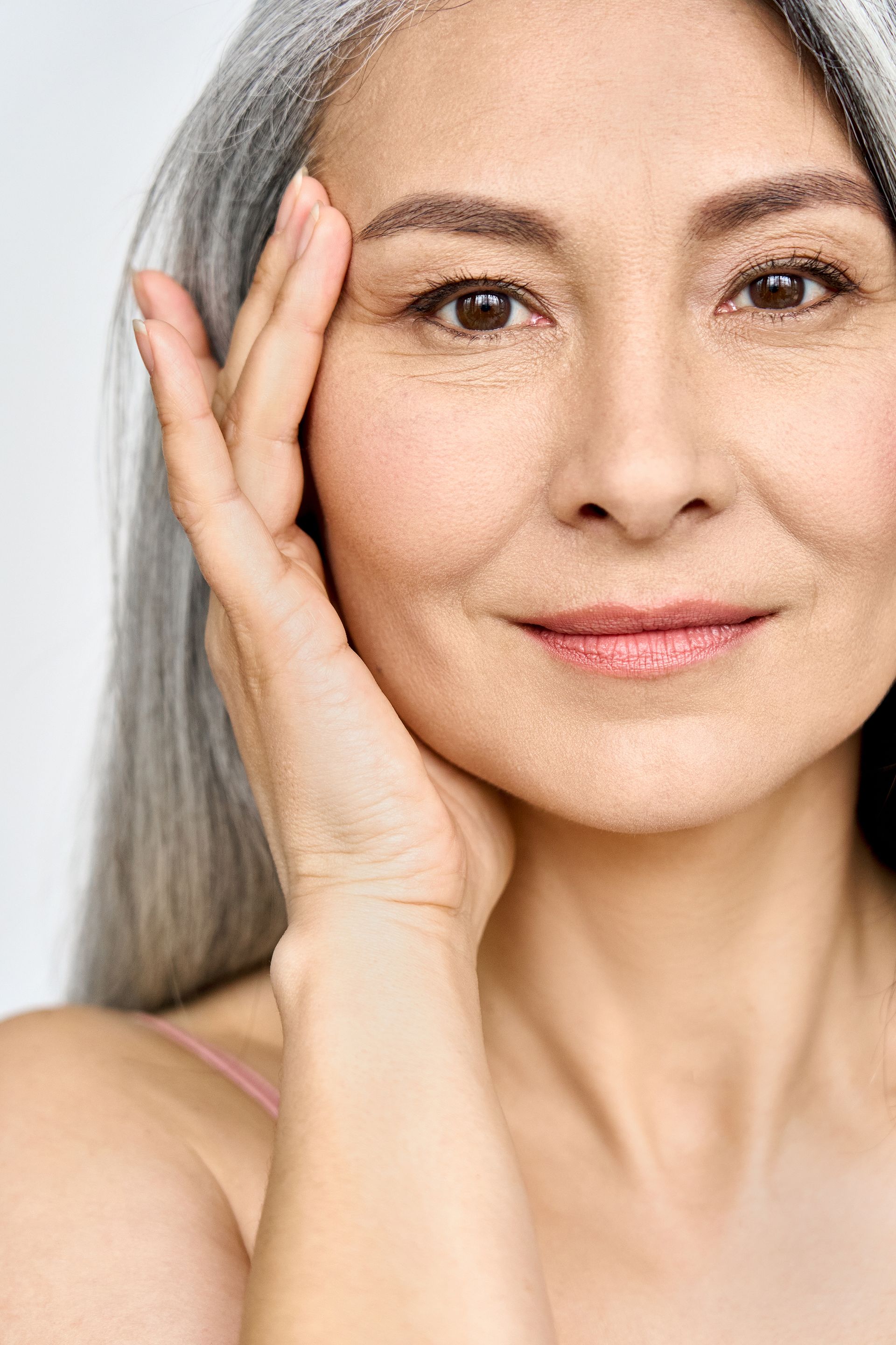A close up of a woman with gray hair touching her face.