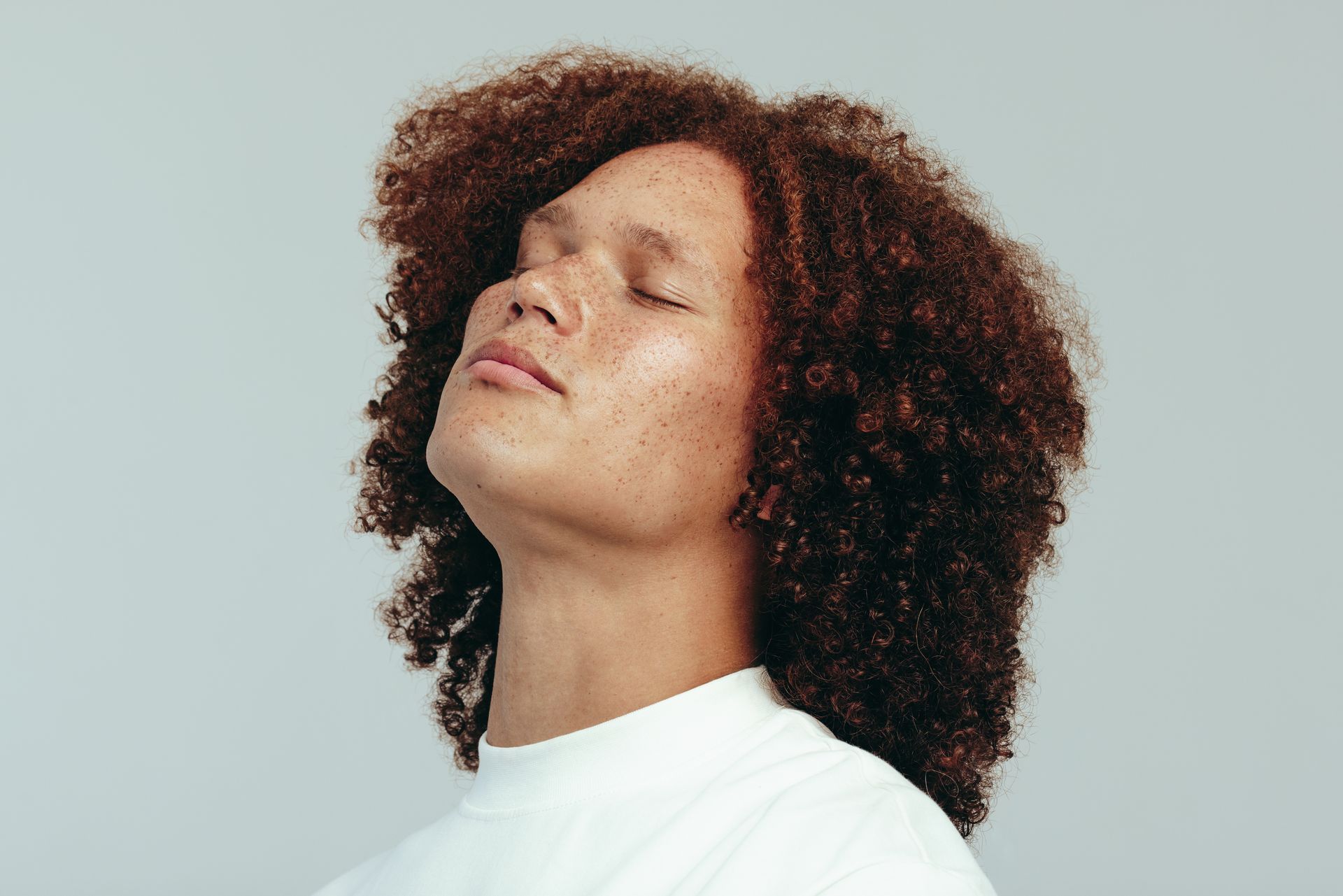 A man with curly hair is looking up with his eyes closed.