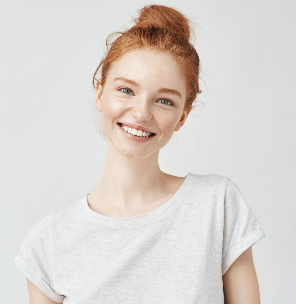 A woman with red hair is wearing a white t-shirt and smiling.