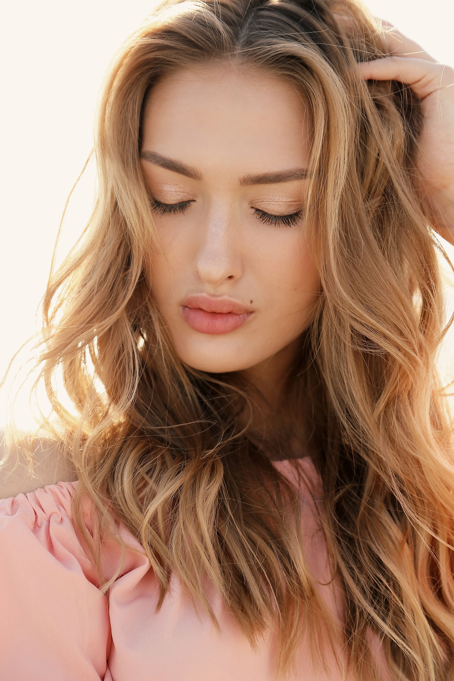 A close up of a woman 's face with her eyes closed and her hand in her hair.