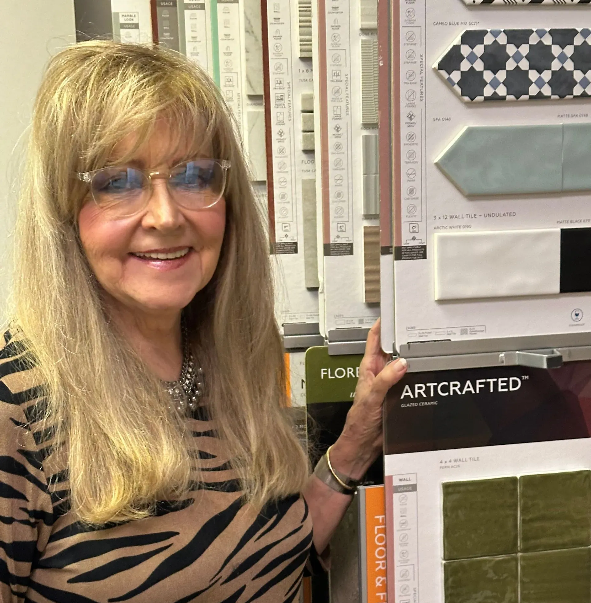 Woman with glasses, smiles while standing by tile samples.