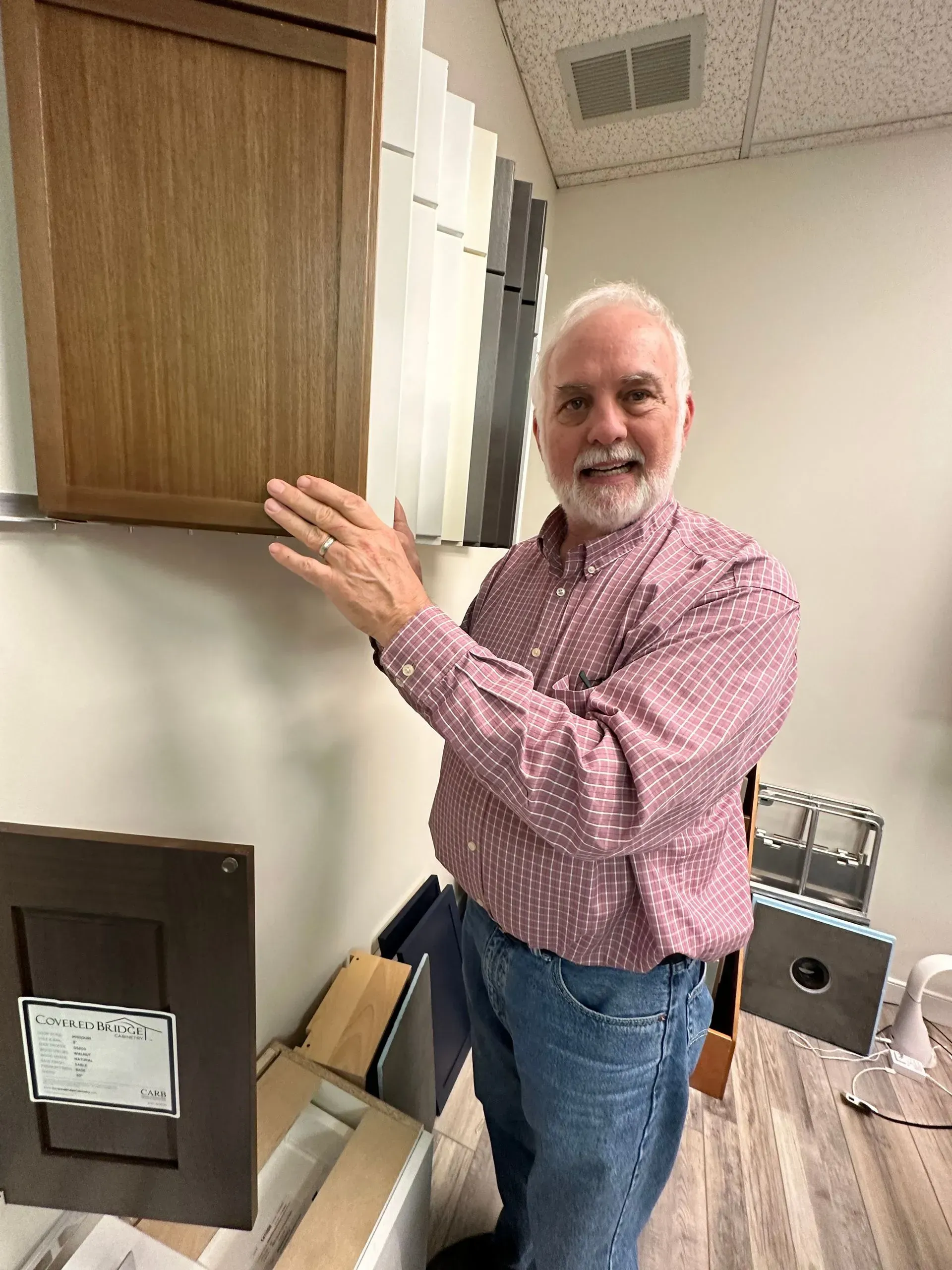 Man in red shirt points to wooden cabinet samples in a showroom.