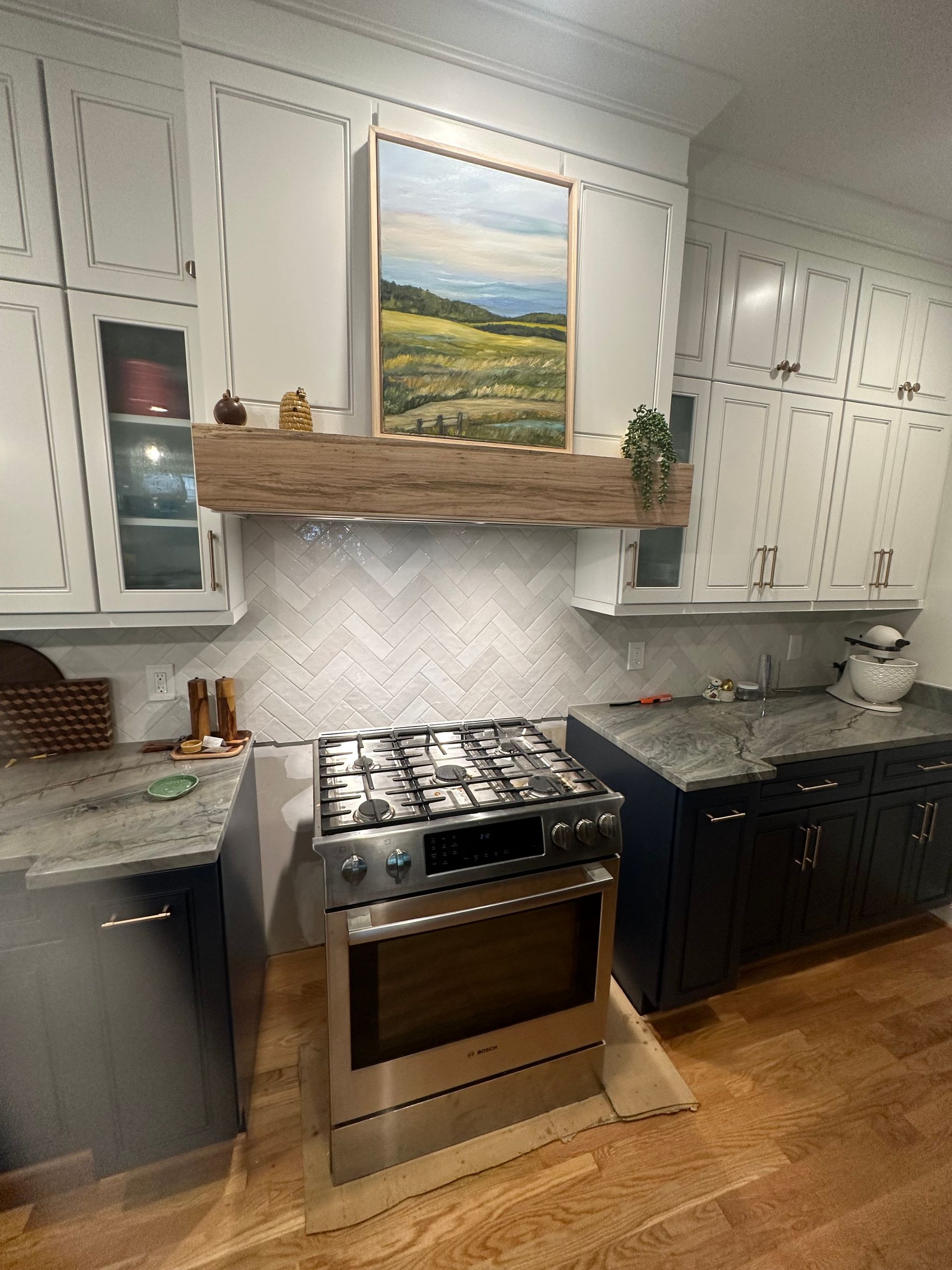 Kitchen with white cabinets, blue and gray countertops, stainless steel stove, and landscape art.