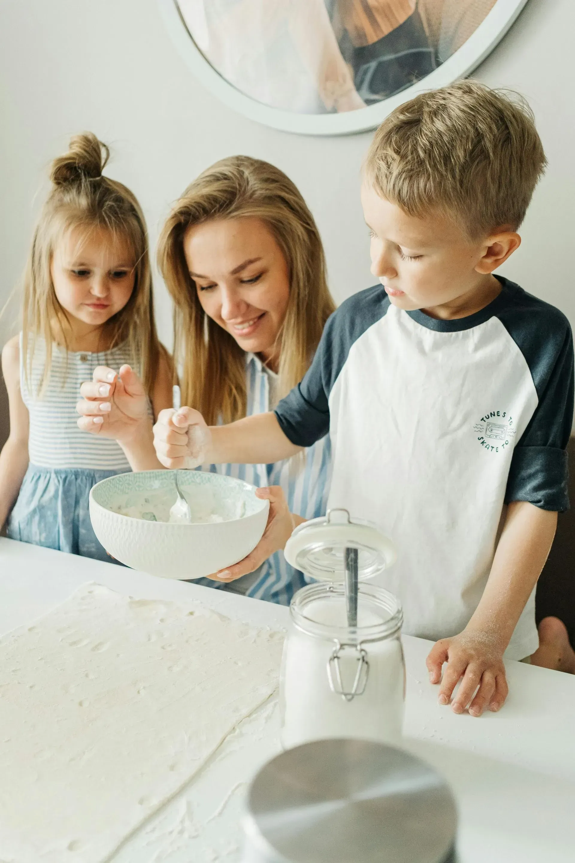 Woman and two children baking together, mixing in a bowl, flour on table.