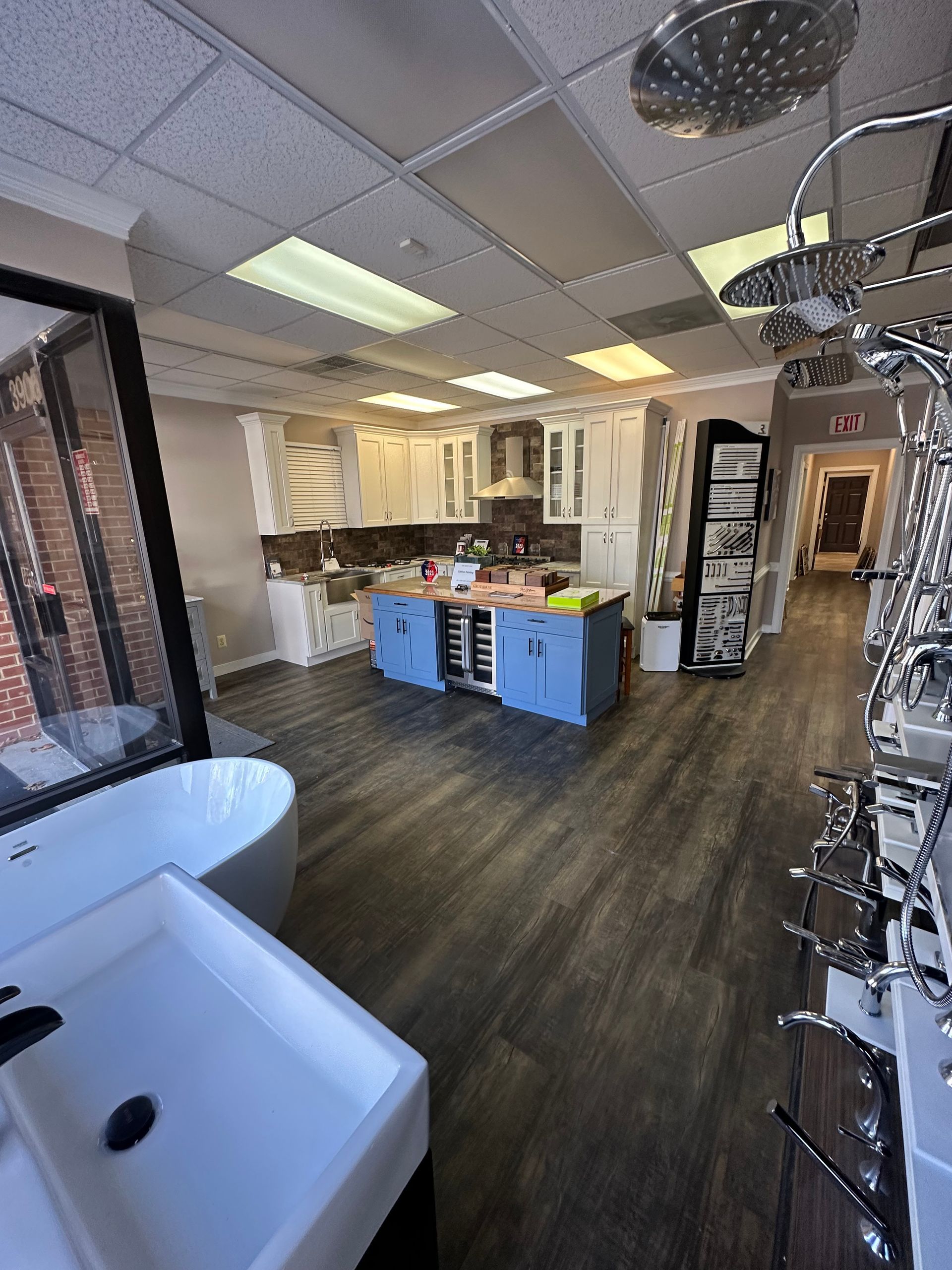 Interior of a showroom with kitchen display and bathroom fixtures. Gray flooring, white cabinets, blue island.