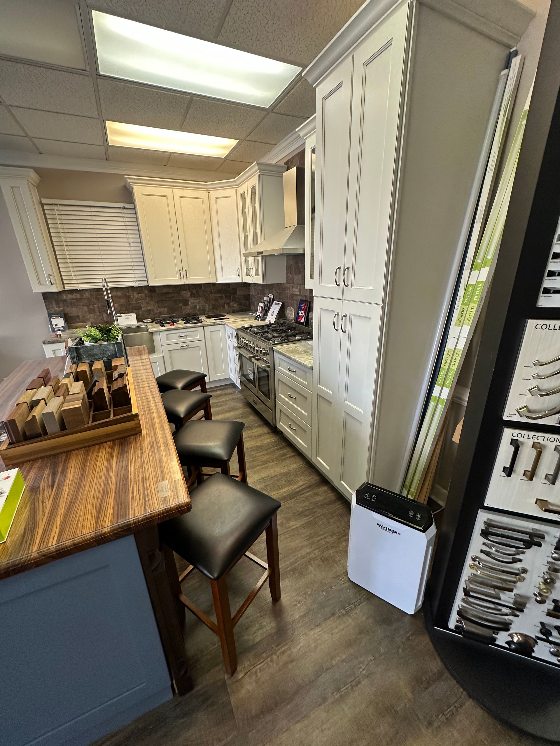 Kitchen showroom with white cabinets, stainless steel appliances, and a wooden bar with stools.