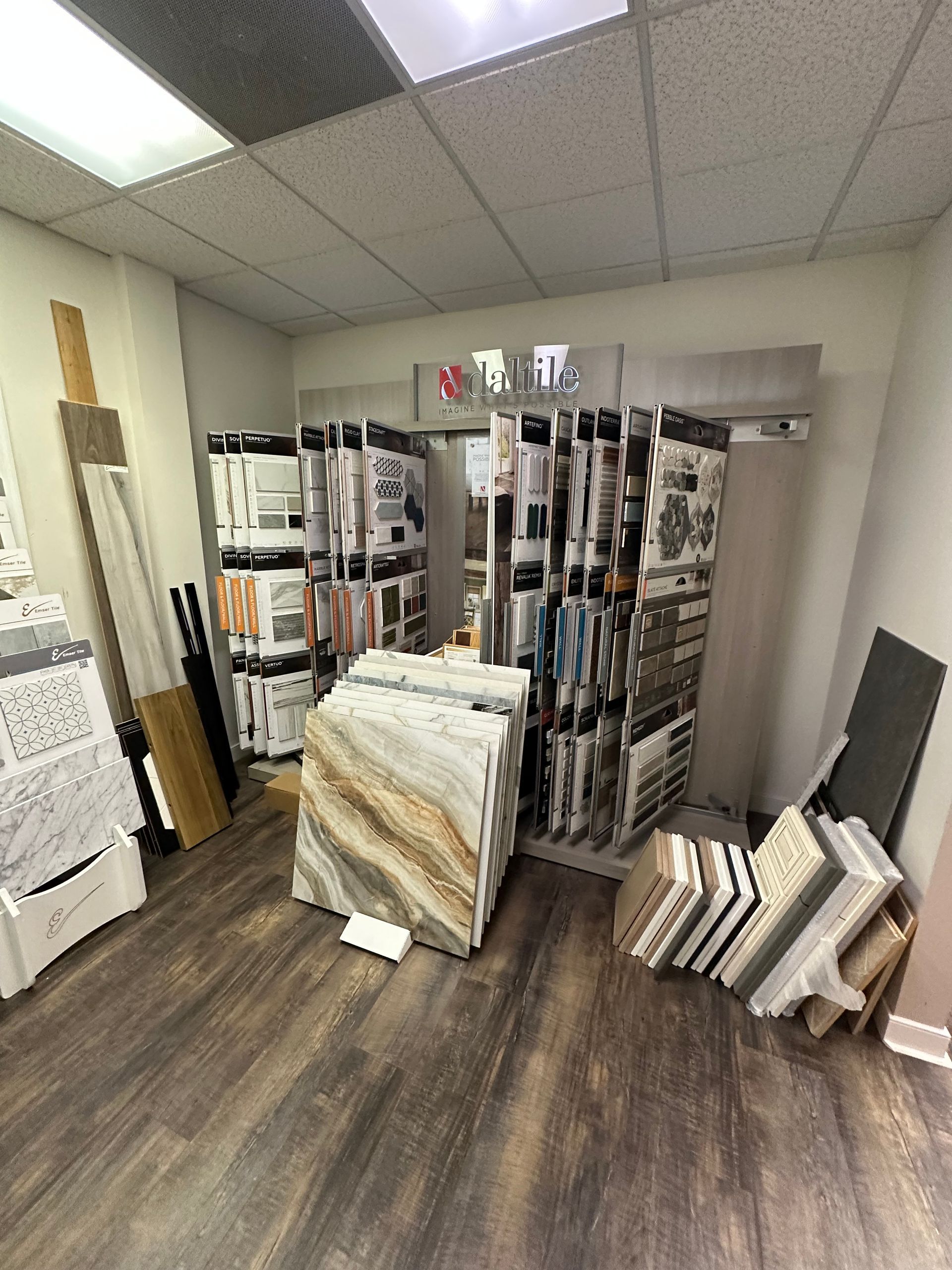 Tile showroom with various tile samples on display against a wall. Wooden floor.