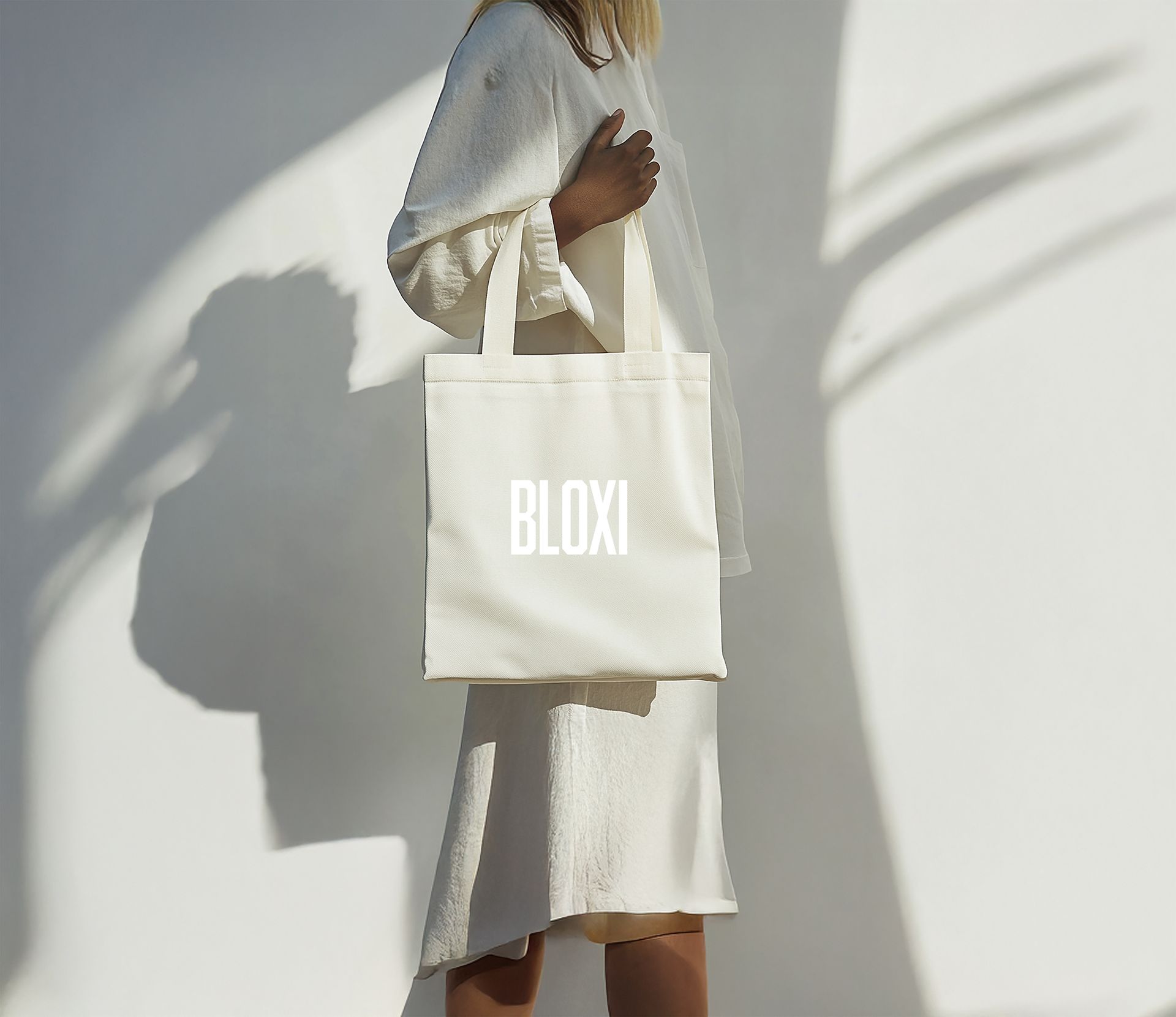 A woman in a white dress is holding a white tote bag that says bloxi