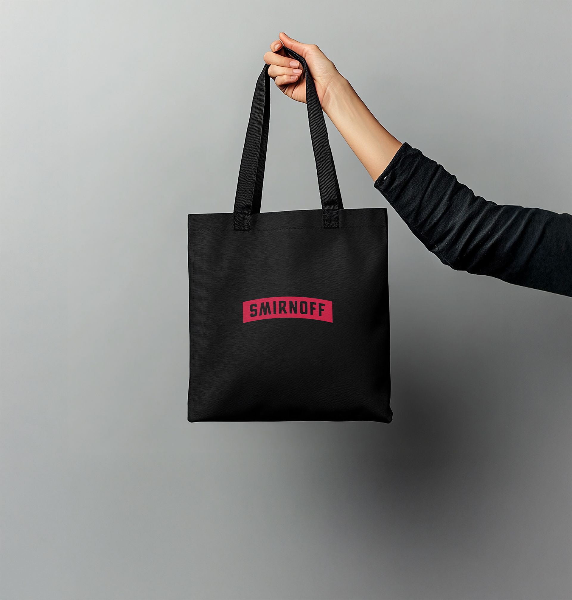 A person is holding a black smirnoff tote bag