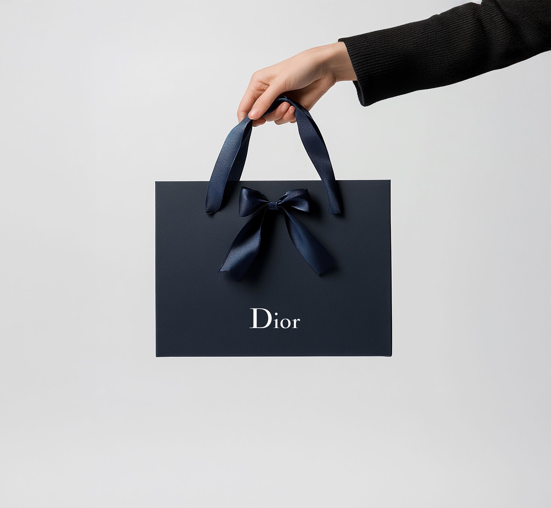 A person is holding a black dior bag with a blue bow.