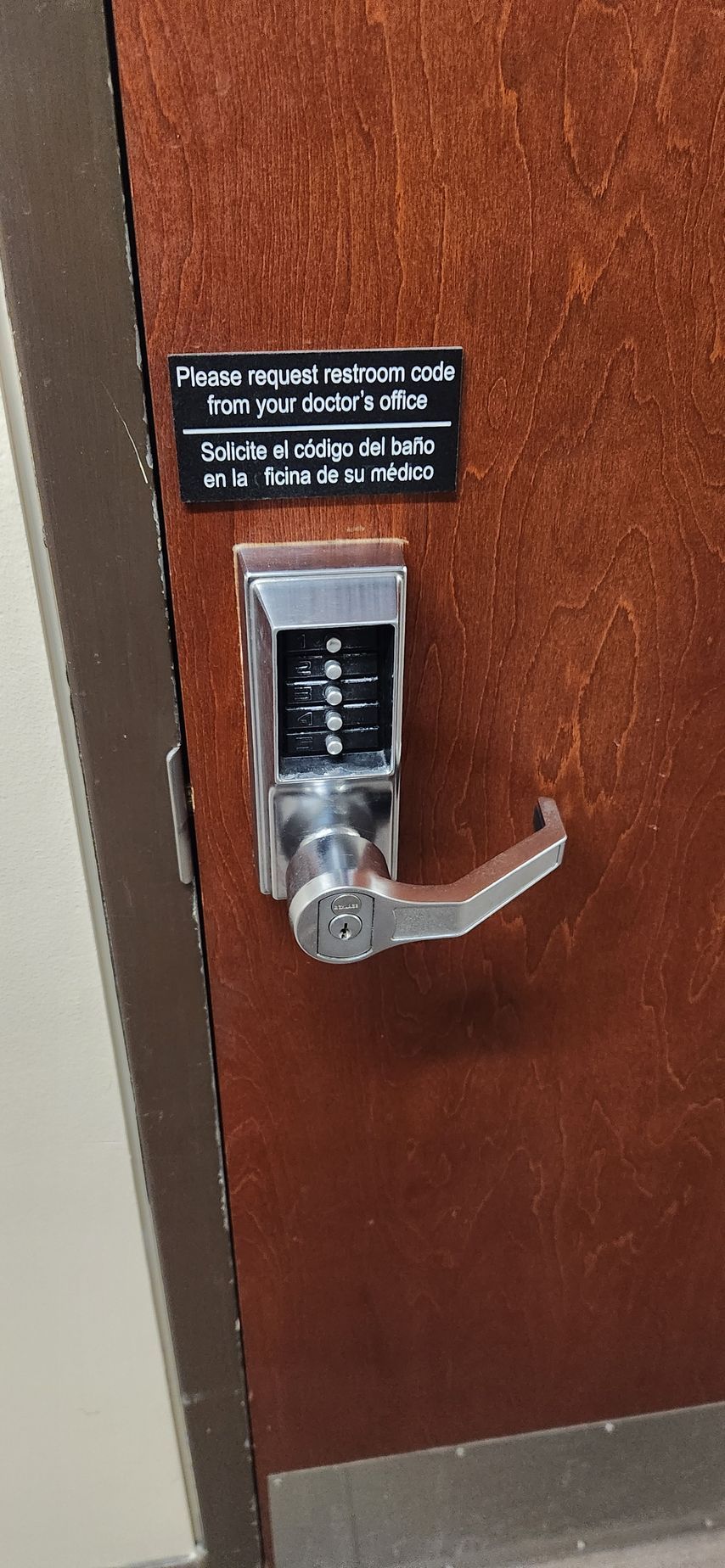 Two men are sitting at a table in front of a door with a digital lock on it.