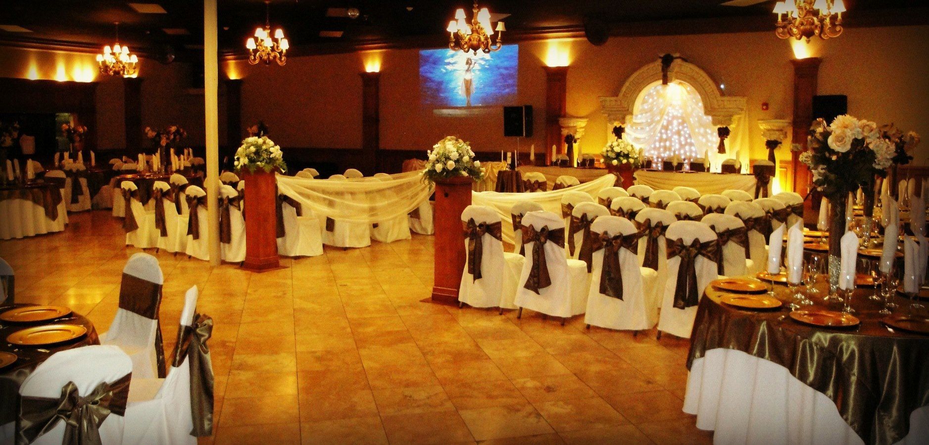 Decorated banquet hall with white chair covers, gold accents, and round tables set for an event