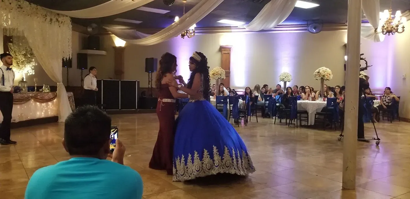 Two women dancing at a formal reception, one in a blue ball gown and one in a burgundy dress.