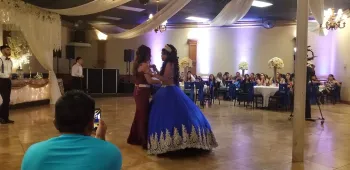 Two women dancing at a formal reception, one in a blue ball gown and one in a burgundy dress.