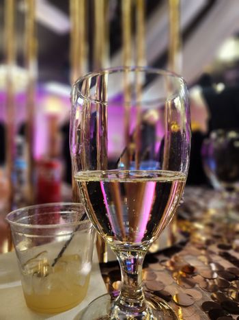 Champagne glass and small cocktail on a table at a softly lit event with purple décor